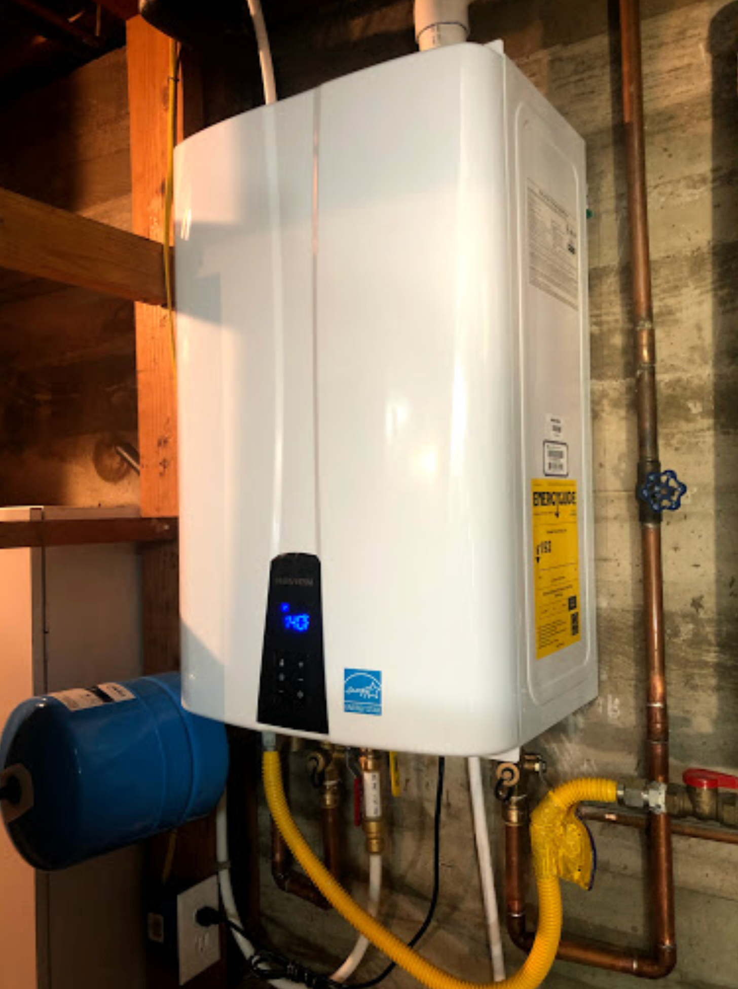 A white water heater is sitting in a basement next to copper pipes.