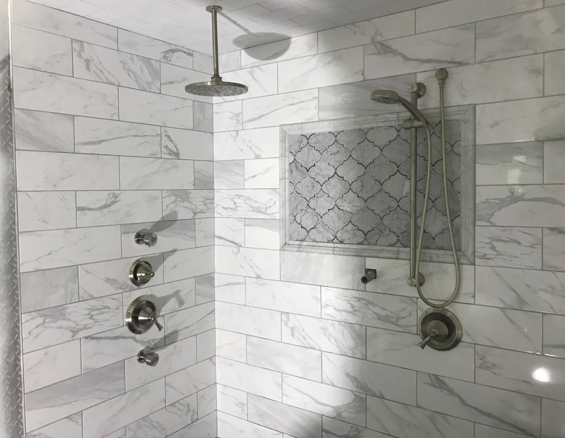 A shower with two shower heads and a marble wall.
