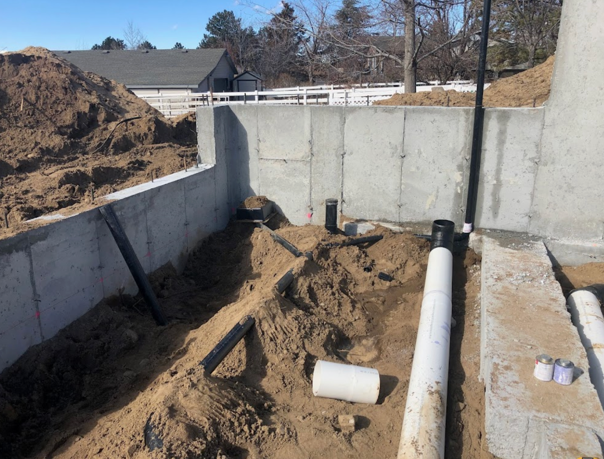 A bunch of pipes are laying in the dirt in front of a concrete wall