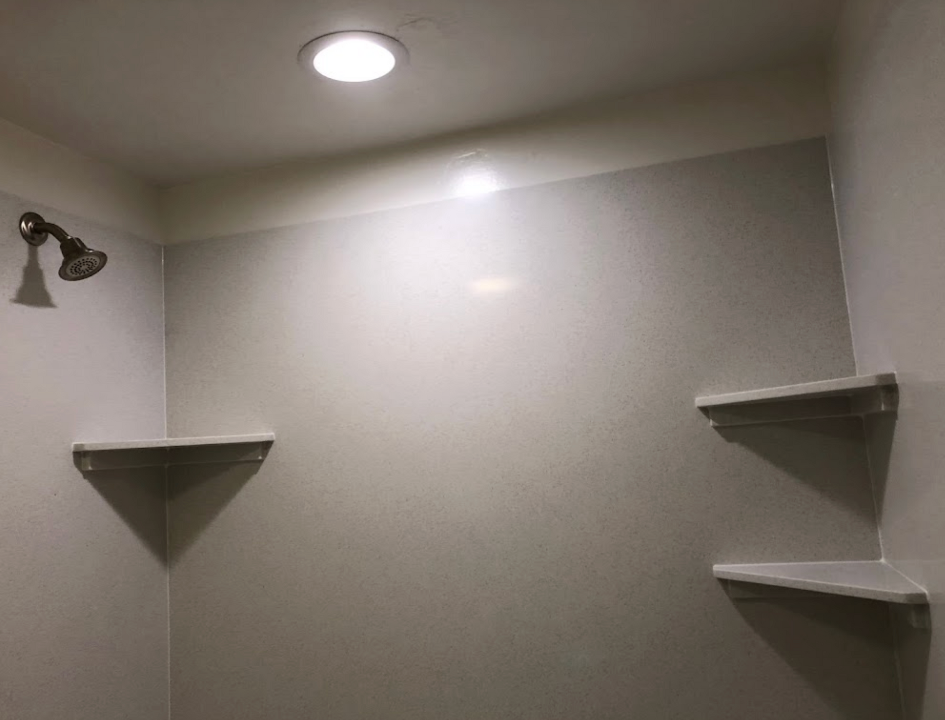 A shower with a shower head and shelves in a bathroom.