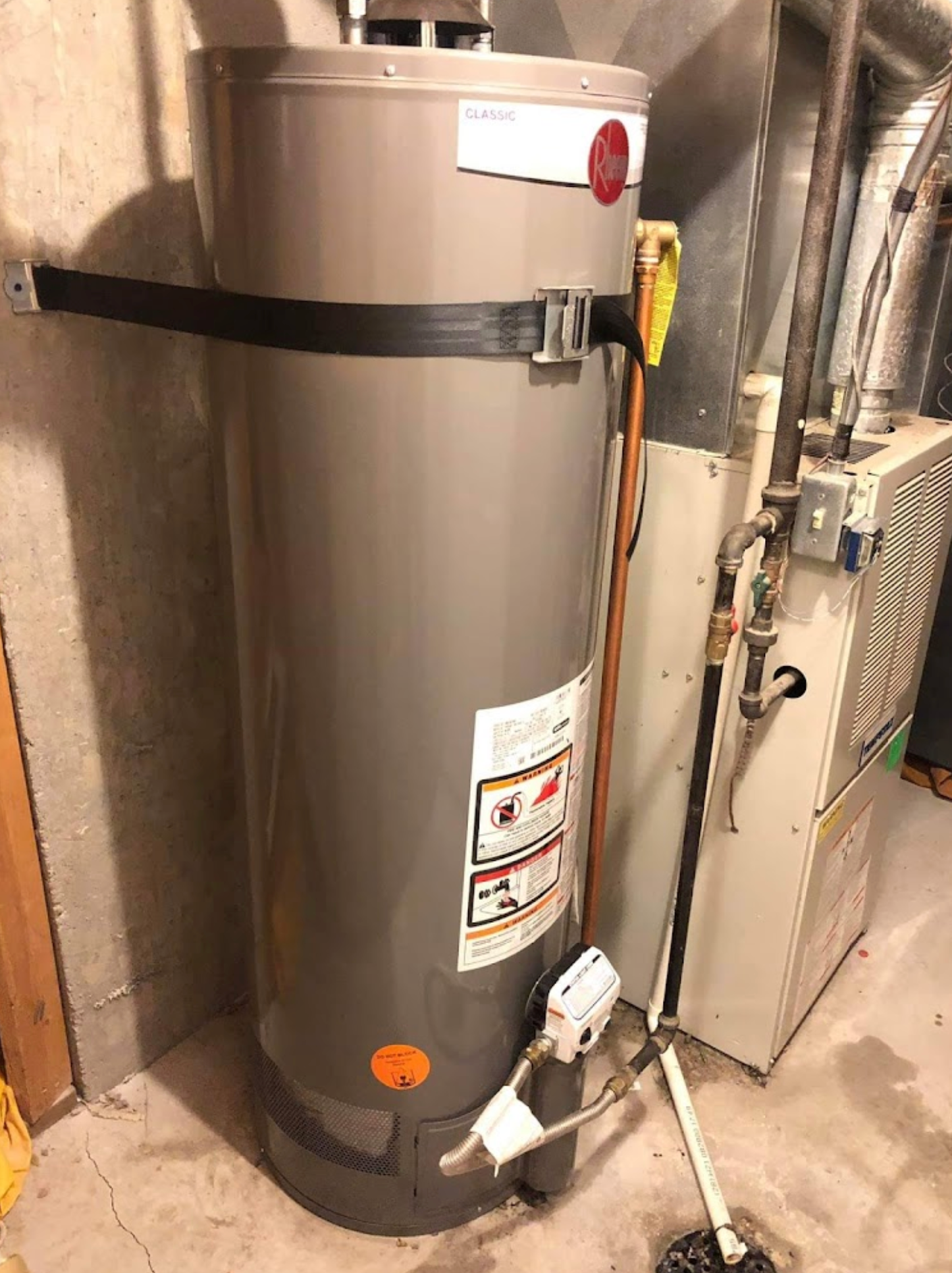 A water heater is sitting next to a furnace in a basement.