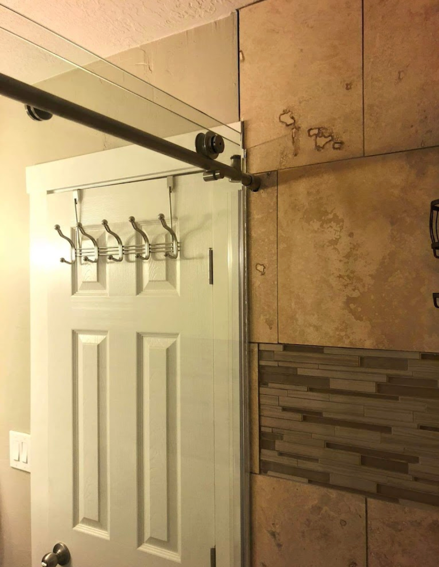 A white door with hooks on it in a bathroom.