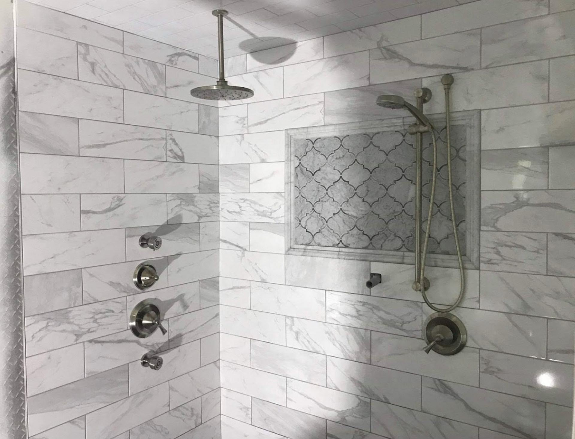 A bathroom with white tiles and a shower head.