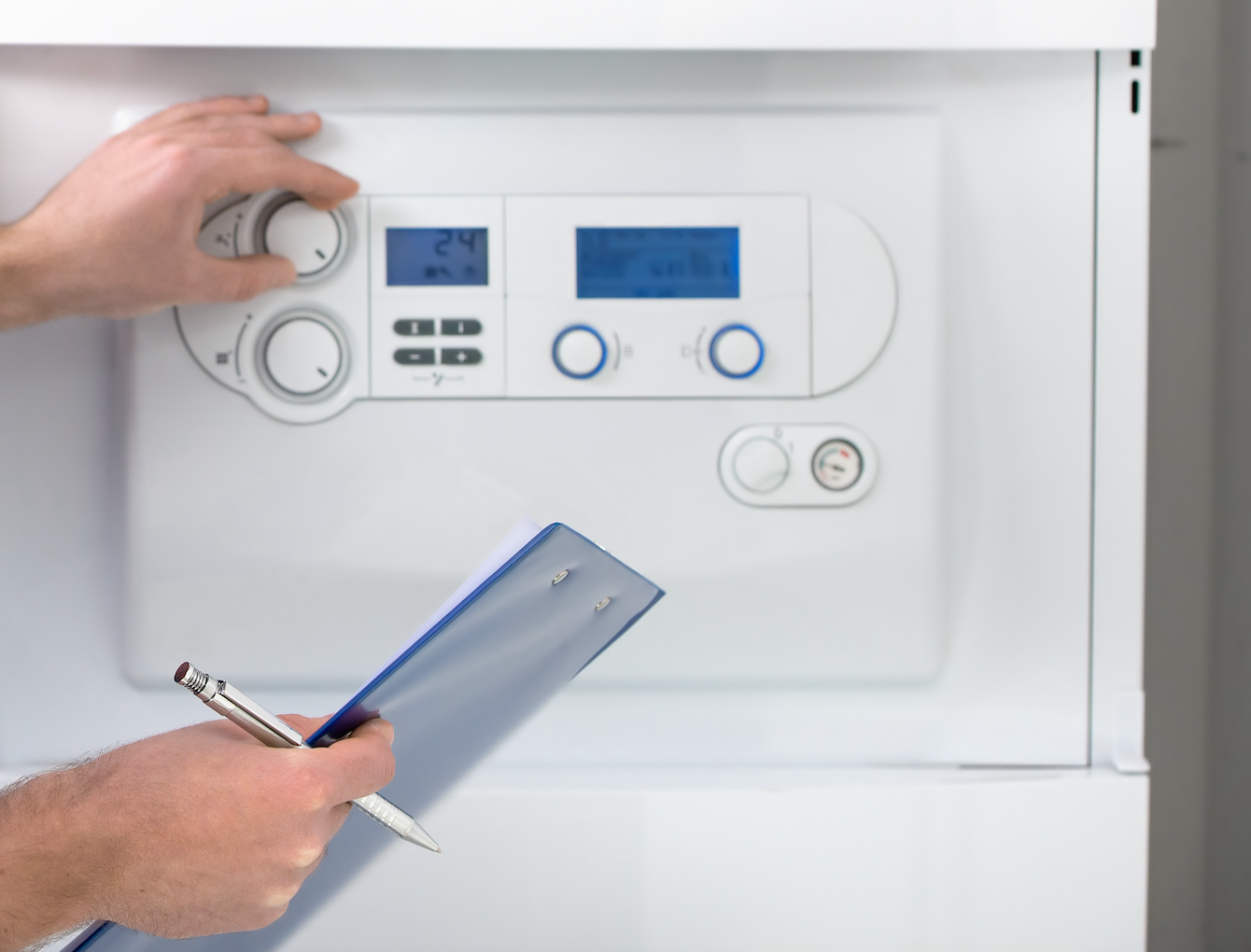 A person is holding a clipboard and a pen in front of a boiler.
