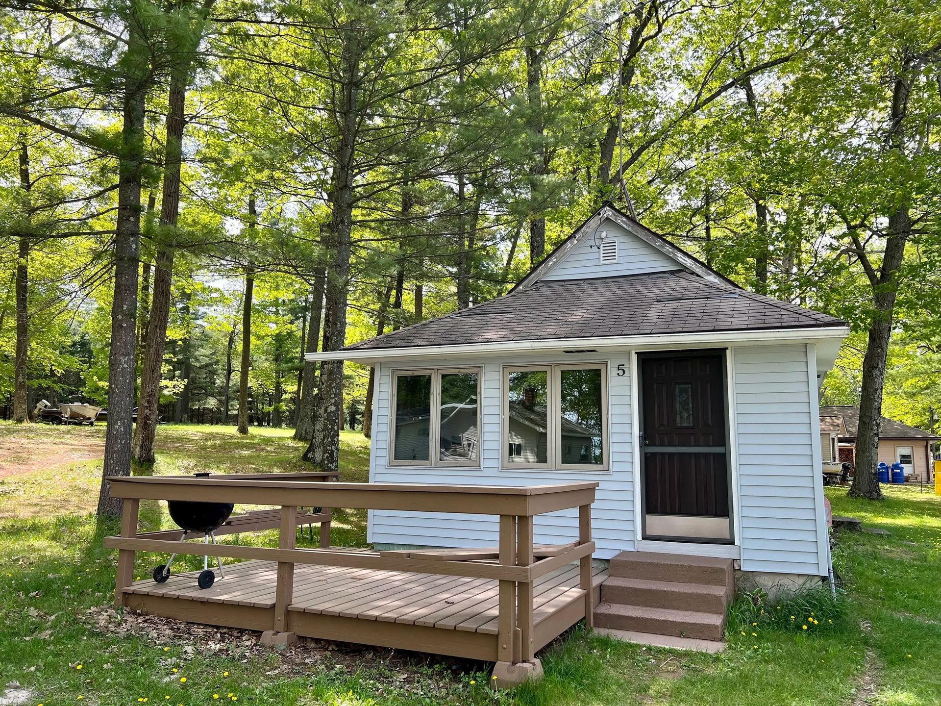 Small, light-blue cottage with windows and a gray patio in front of trees.