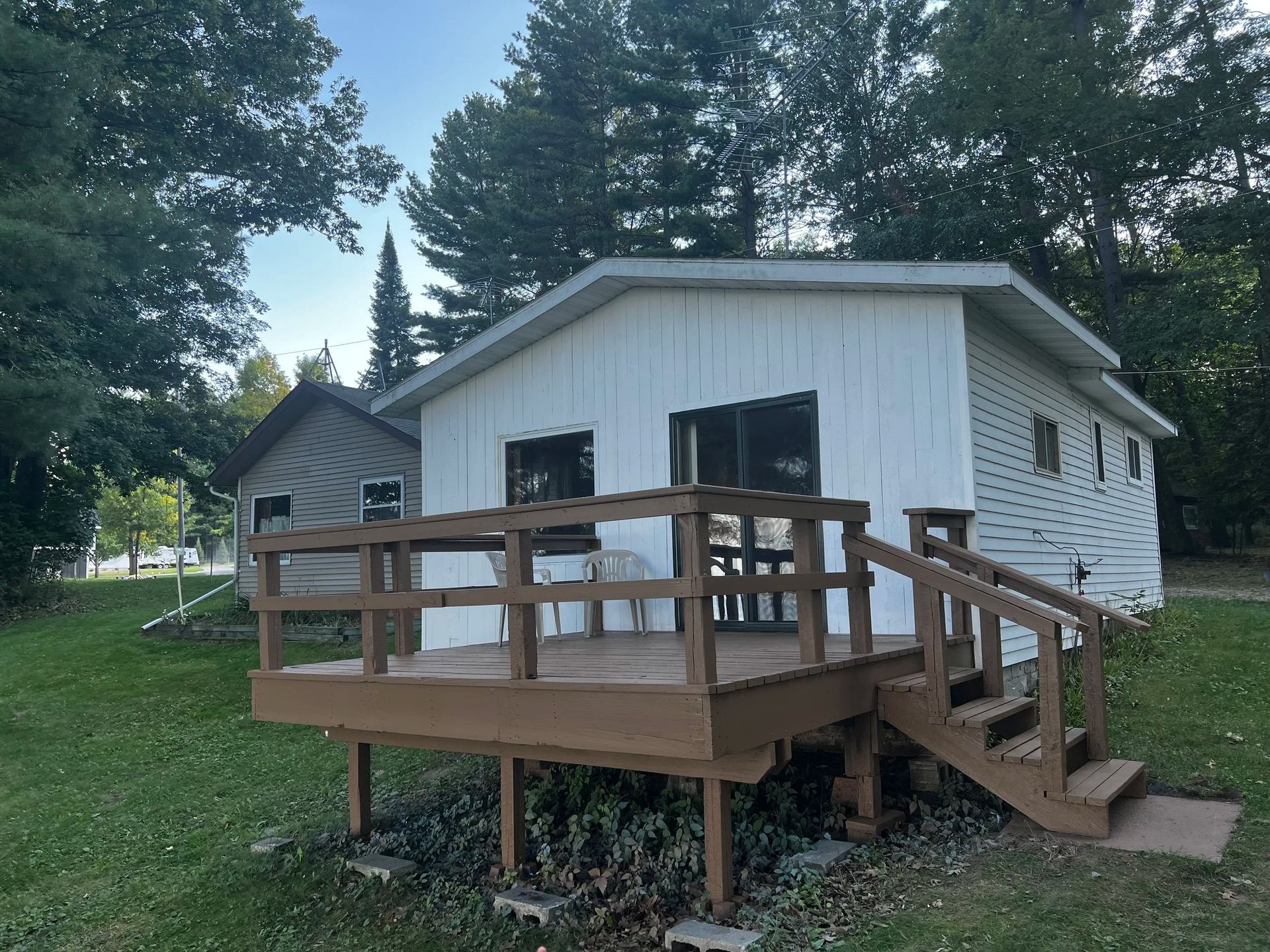 White cabin with brown deck and stairs, on a green lawn.