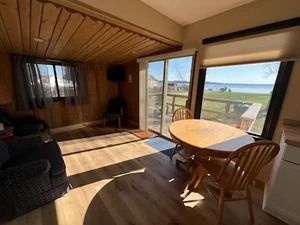 Cozy cabin interior with wooden walls, a dining table, and a large window overlooking a body of water.