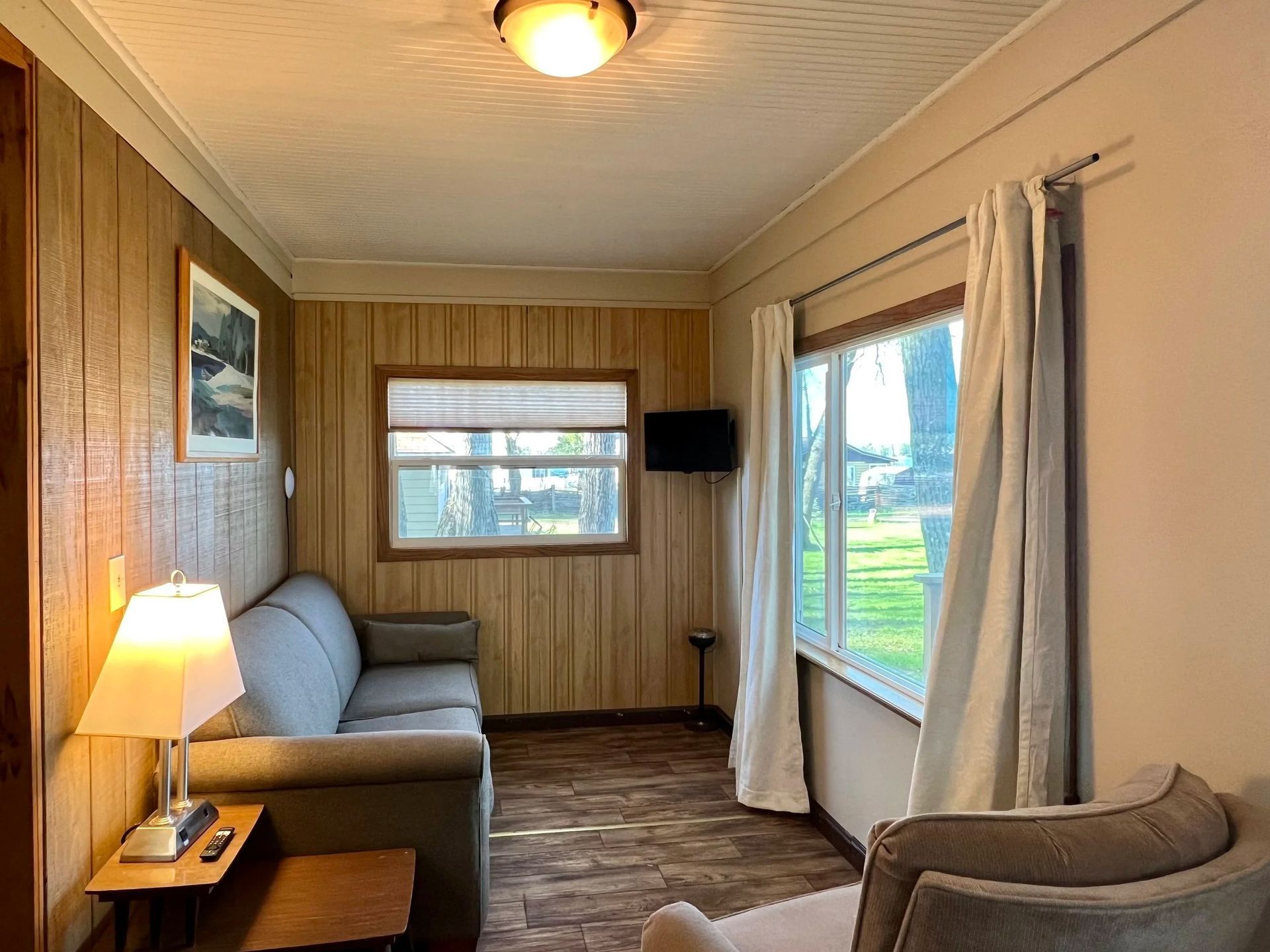 Small, light-blue cottage with windows and a gray patio in front of trees.