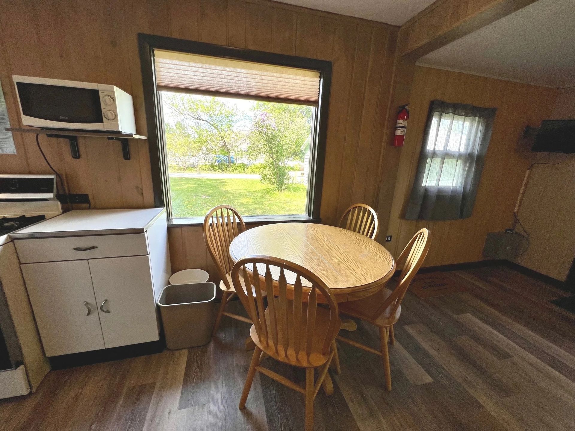 Interior dining area with wooden table, chairs, window, and appliances like a microwave and stove.