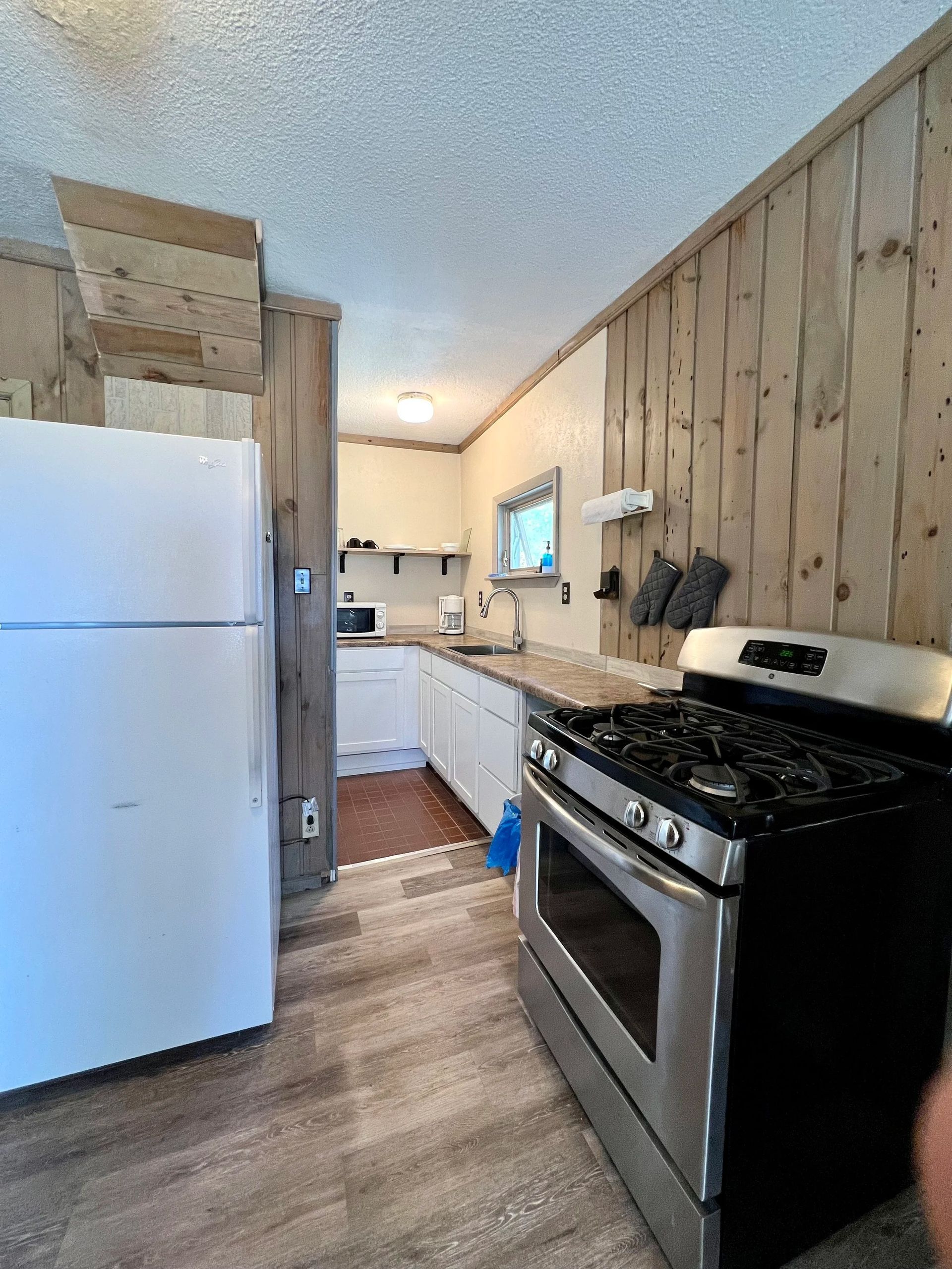 Kitchen with white refrigerator, stainless steel stove, wood-paneled walls, and white cabinets.