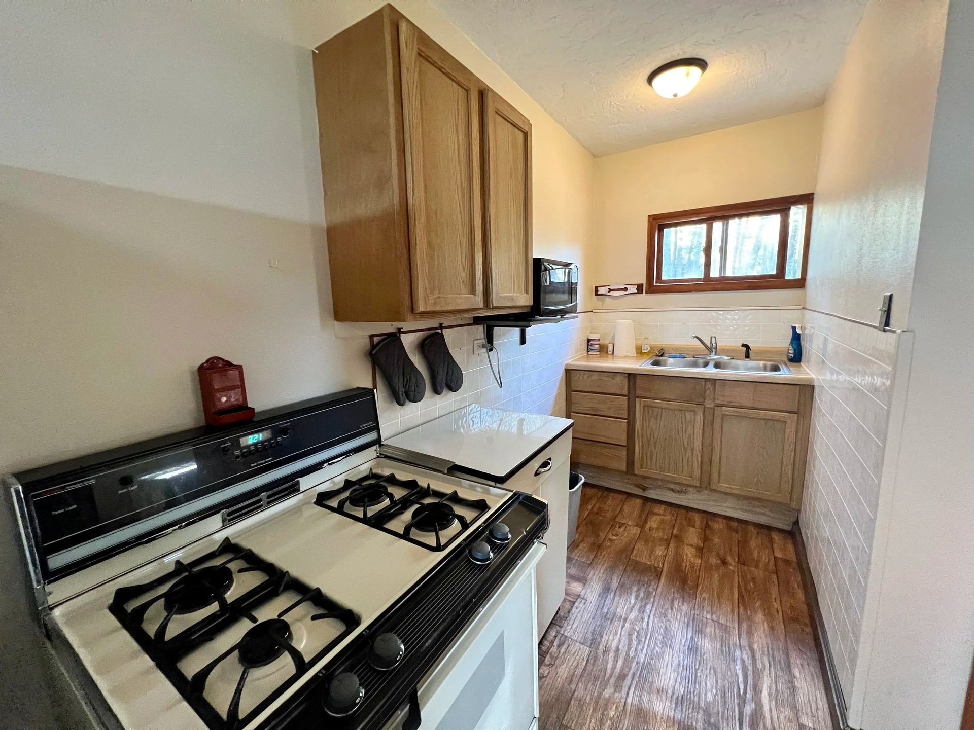 Small kitchen with a stove, cabinets, sink, and a window.