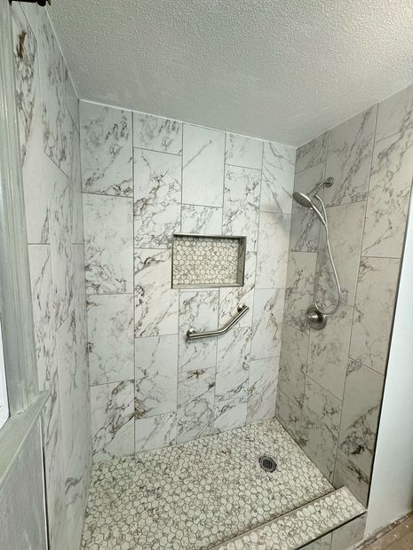 A walk in shower with marble tiles and a hand rail.