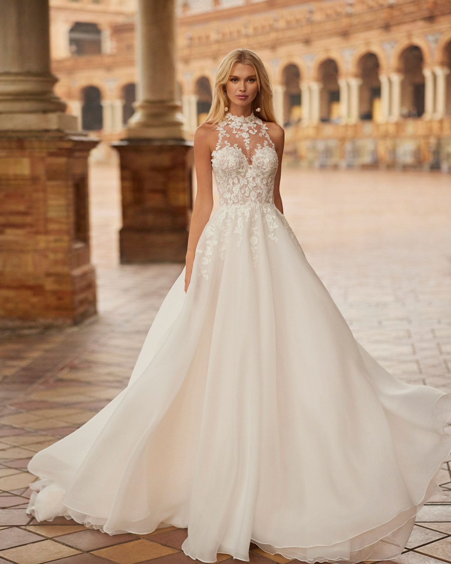 Donna bionda con un abito da sposa bianco, in piedi all'aperto davanti a un edificio decorato.