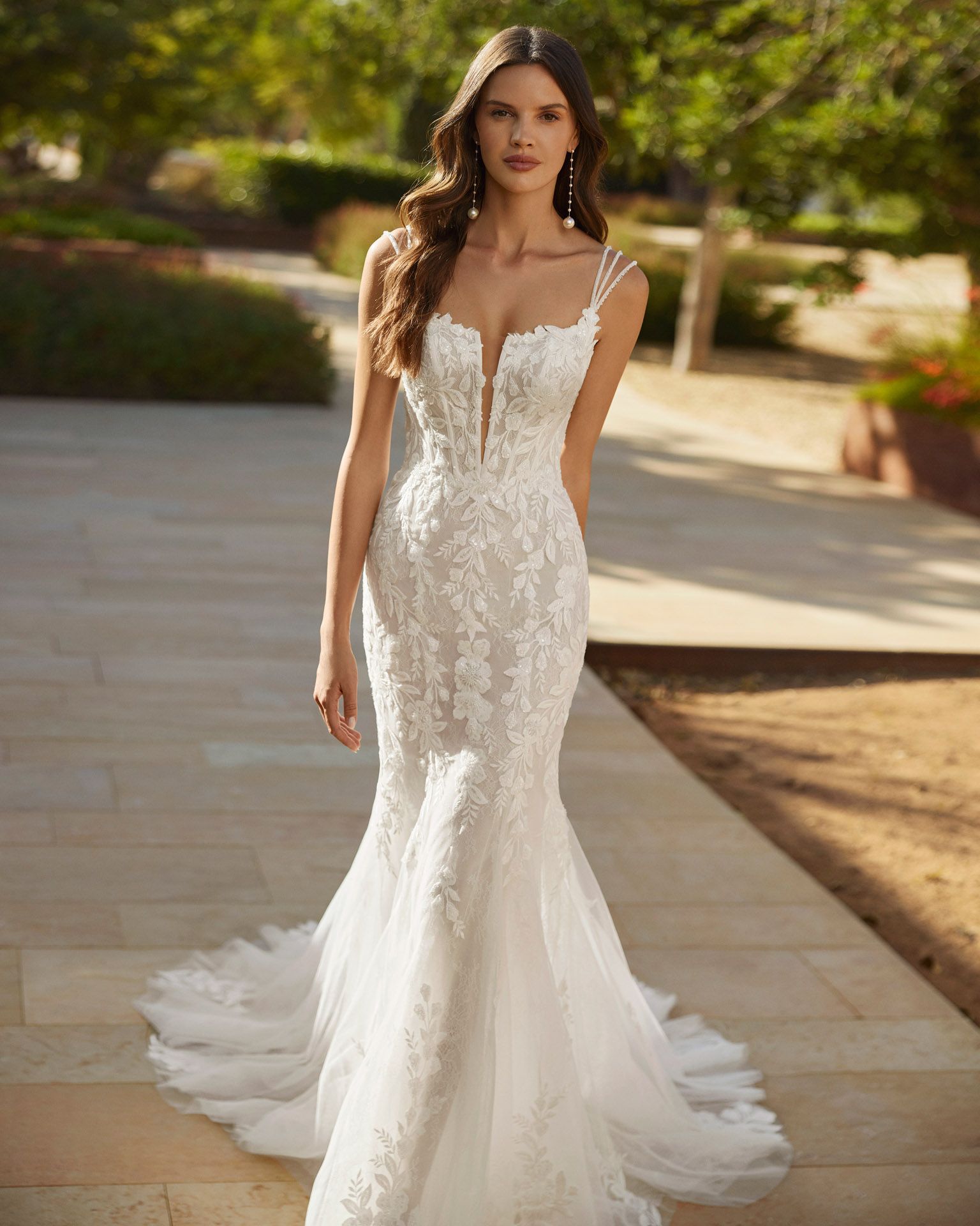 Donna con abito da sposa bianco a sirena con dettagli in pizzo, all'aperto in un giardino.