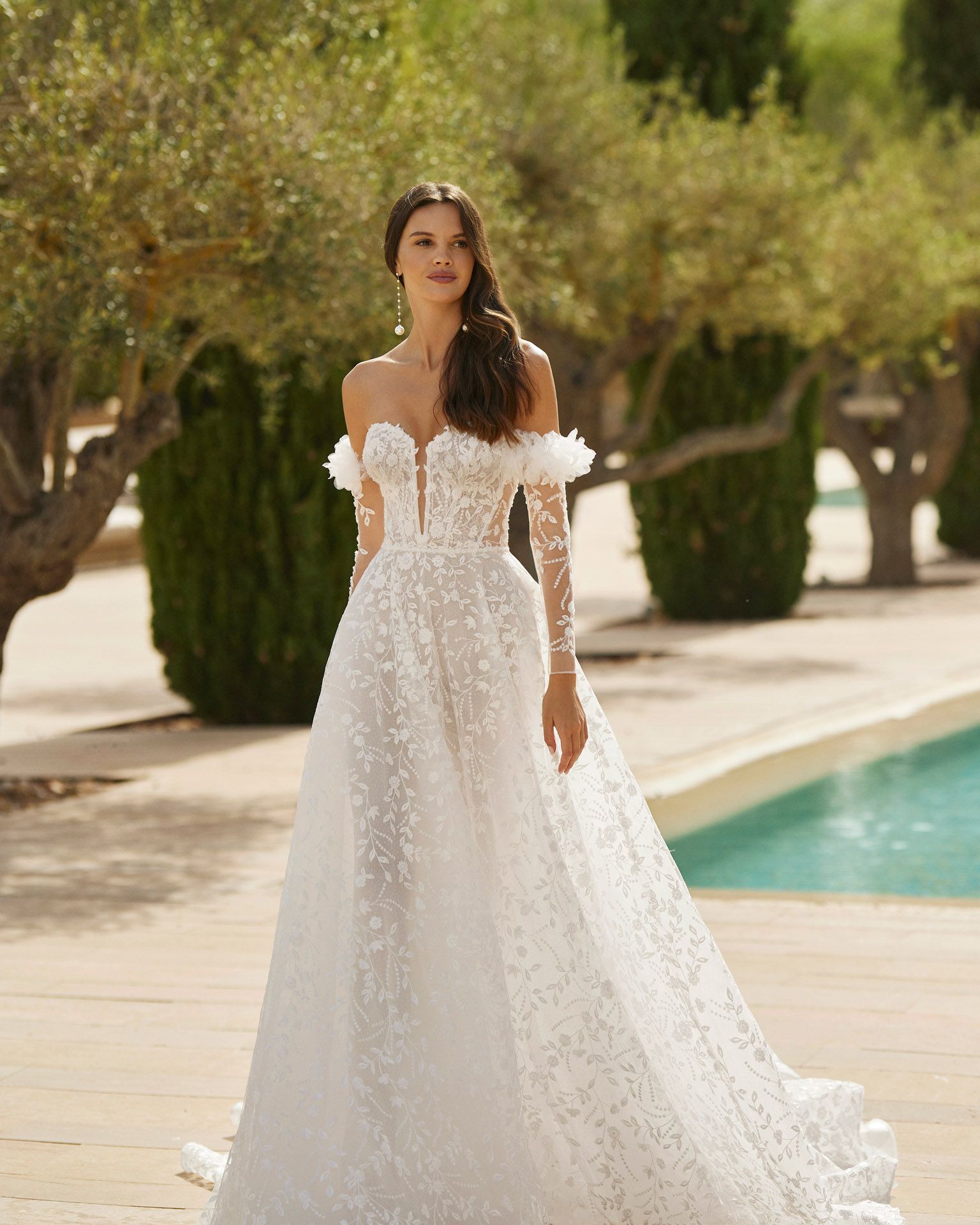 Donna con abito da sposa bianco a fiori, in piedi all'aperto vicino a una piscina.