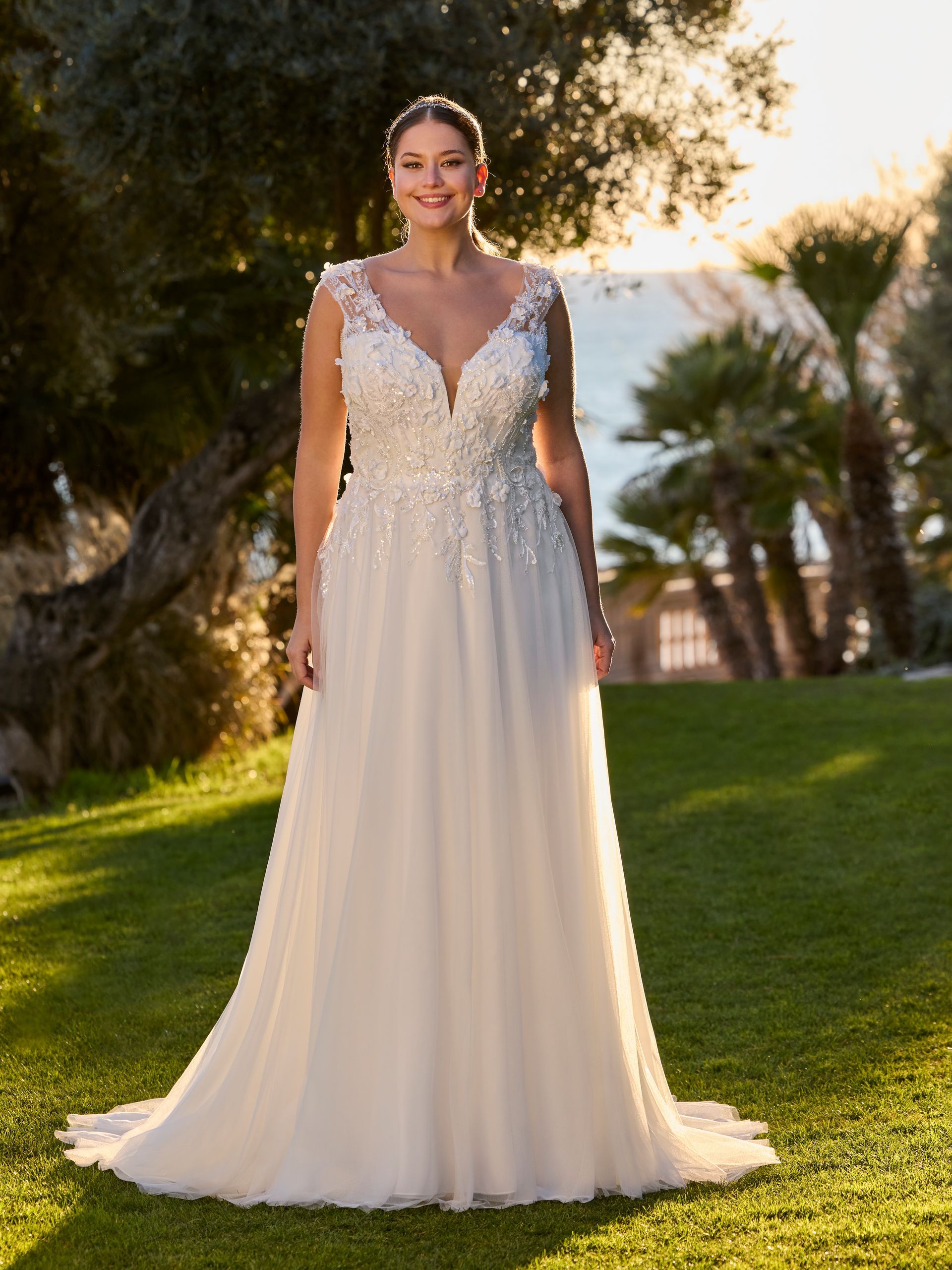 Una donna con un abito da sposa bianco sorride all'aperto, vicino all'acqua.