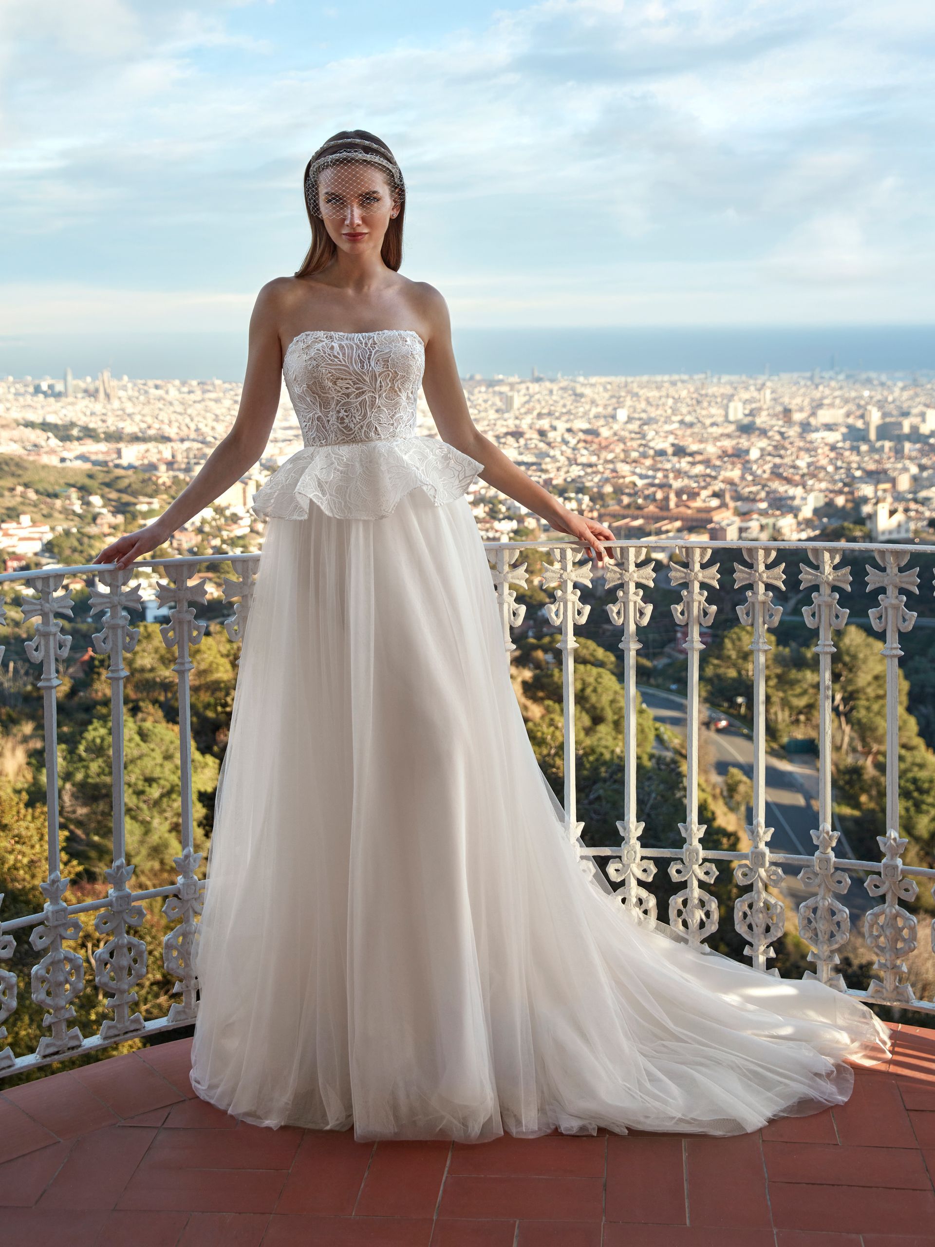 Donna in abito da sposa bianco sul balcone con vista sulla città.