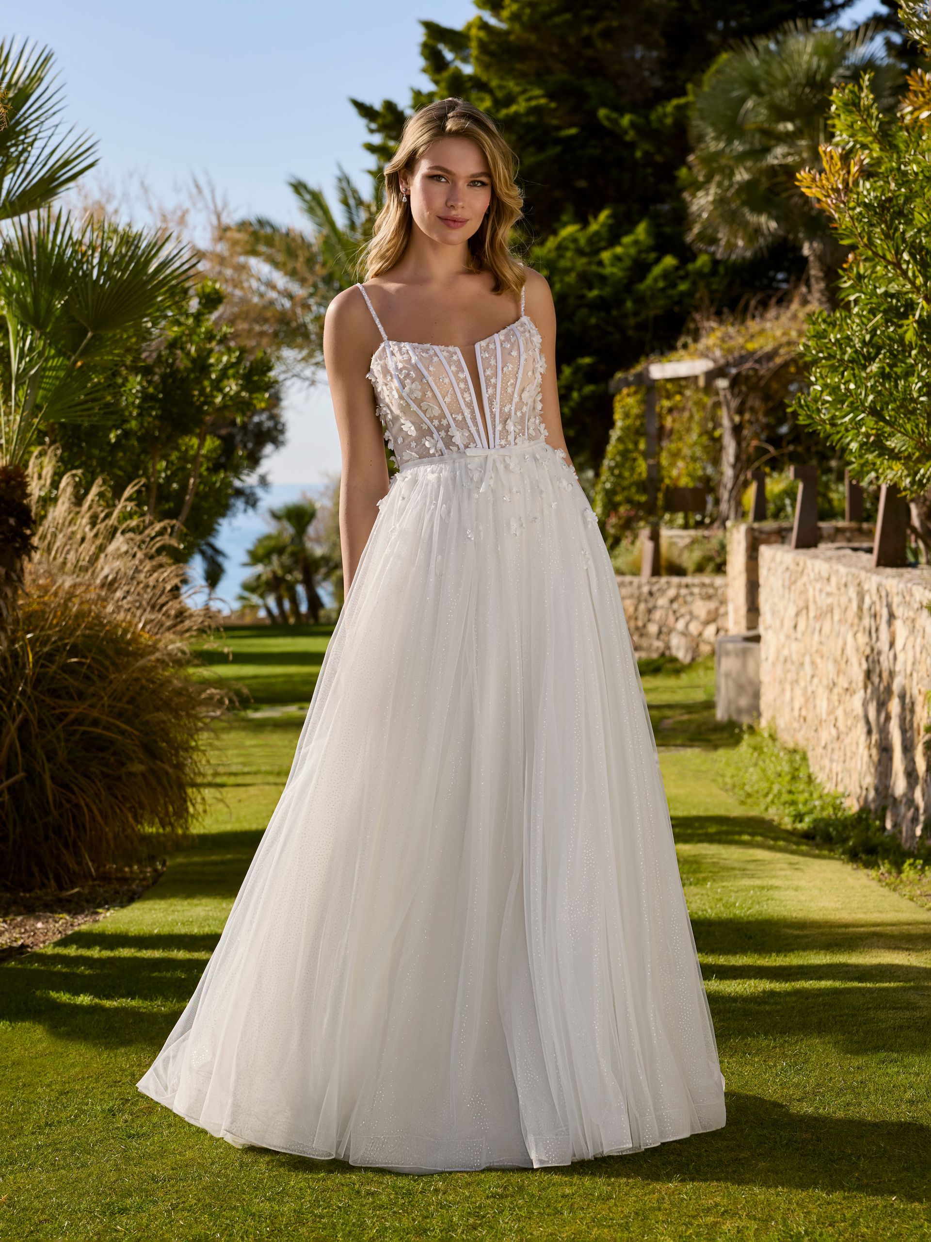 Donna in abito da sposa bianco con corpetto decorato e gonna svolazzante, all'aperto in una giornata di sole.