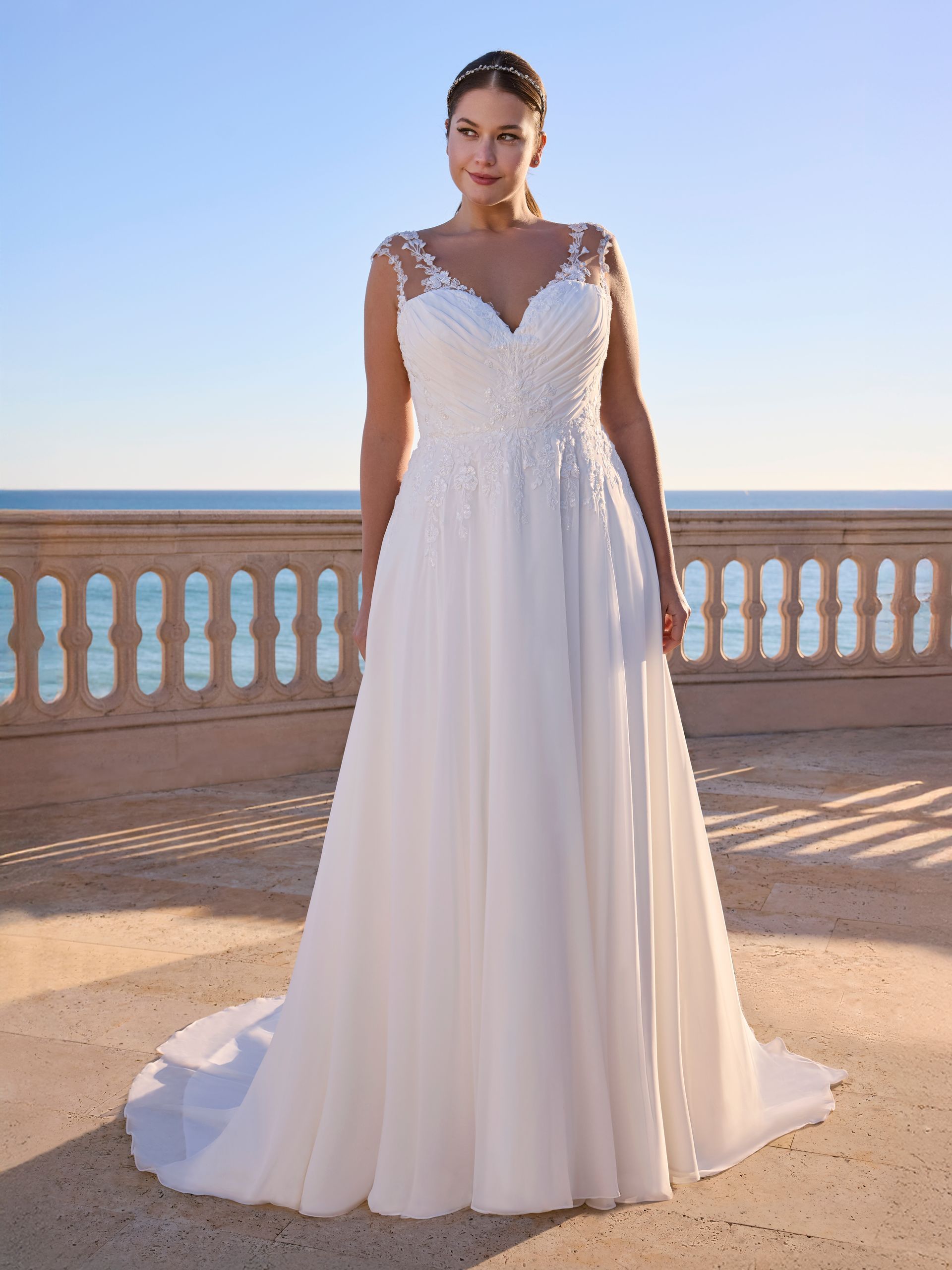 Donna in abito da sposa bianco con dettagli floreali, in piedi all'aperto.