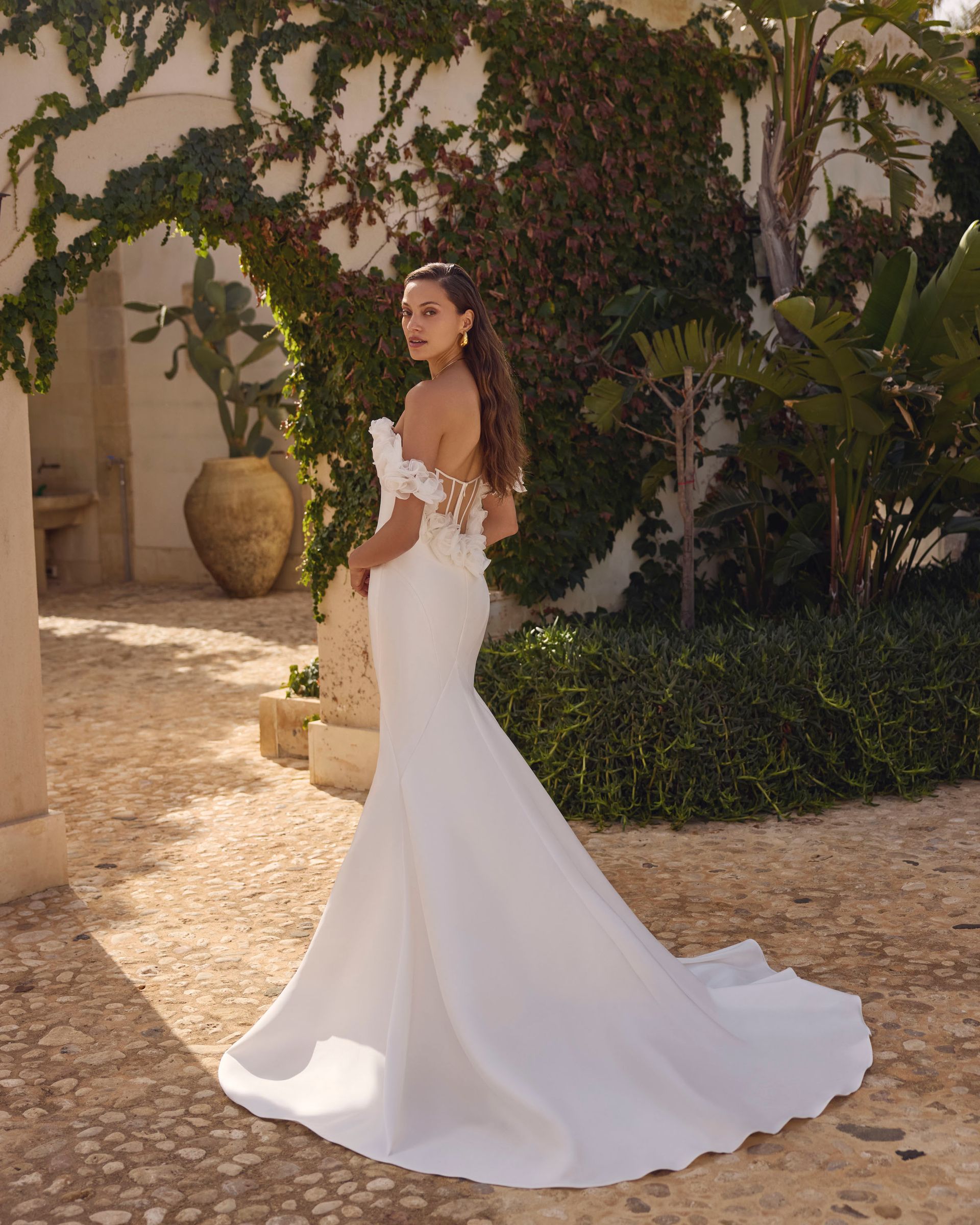 Una donna in abito da sposa bianco posa all'aperto, guardando indietro, con uno strascico.