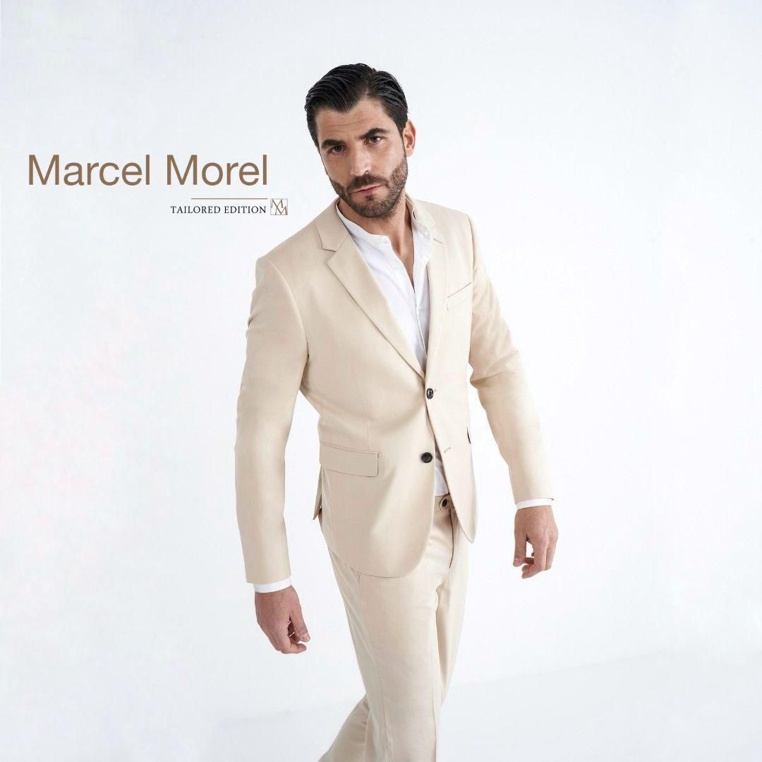 Marcel Morel in abito beige, appoggiato, in studio.