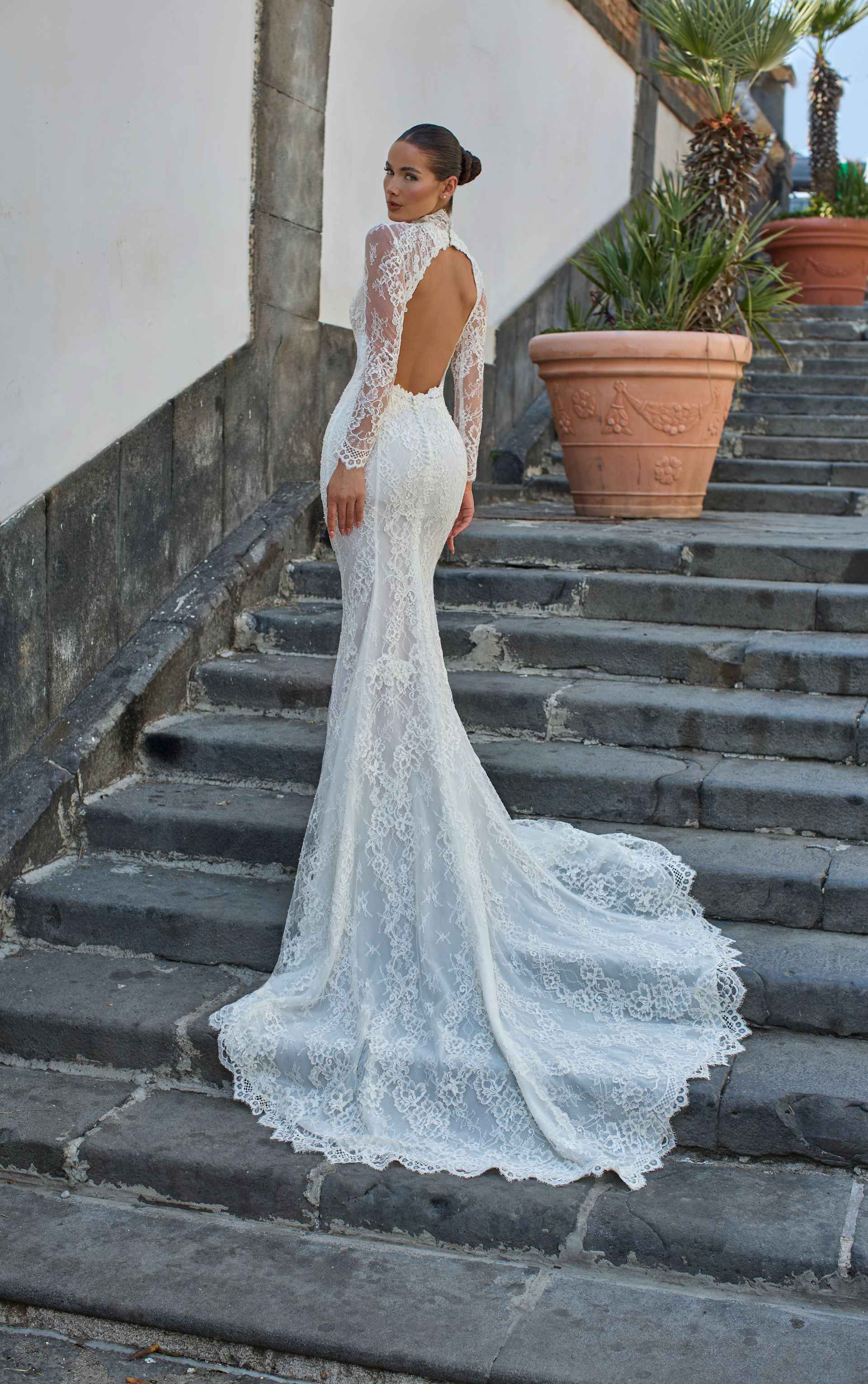 Donna in abito da sposa in pizzo bianco su gradini di pietra.