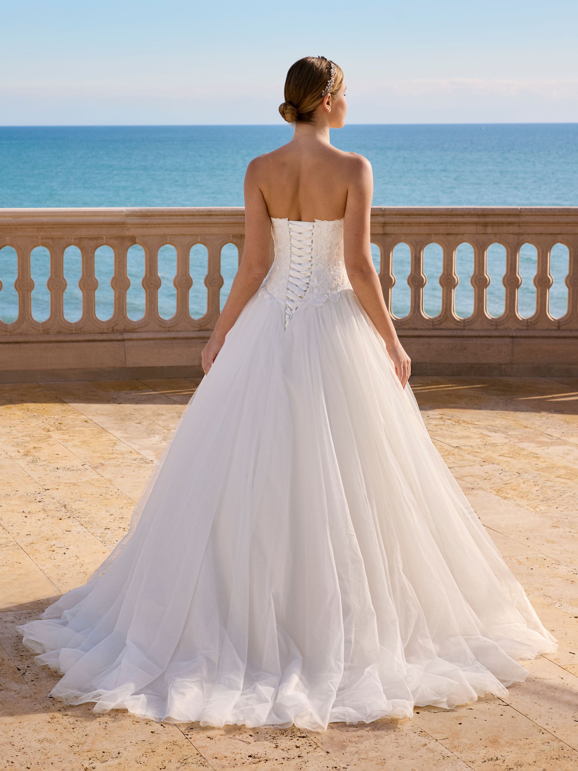 Sposa in abito bianco senza spalline su una terrazza con vista sull'oceano.