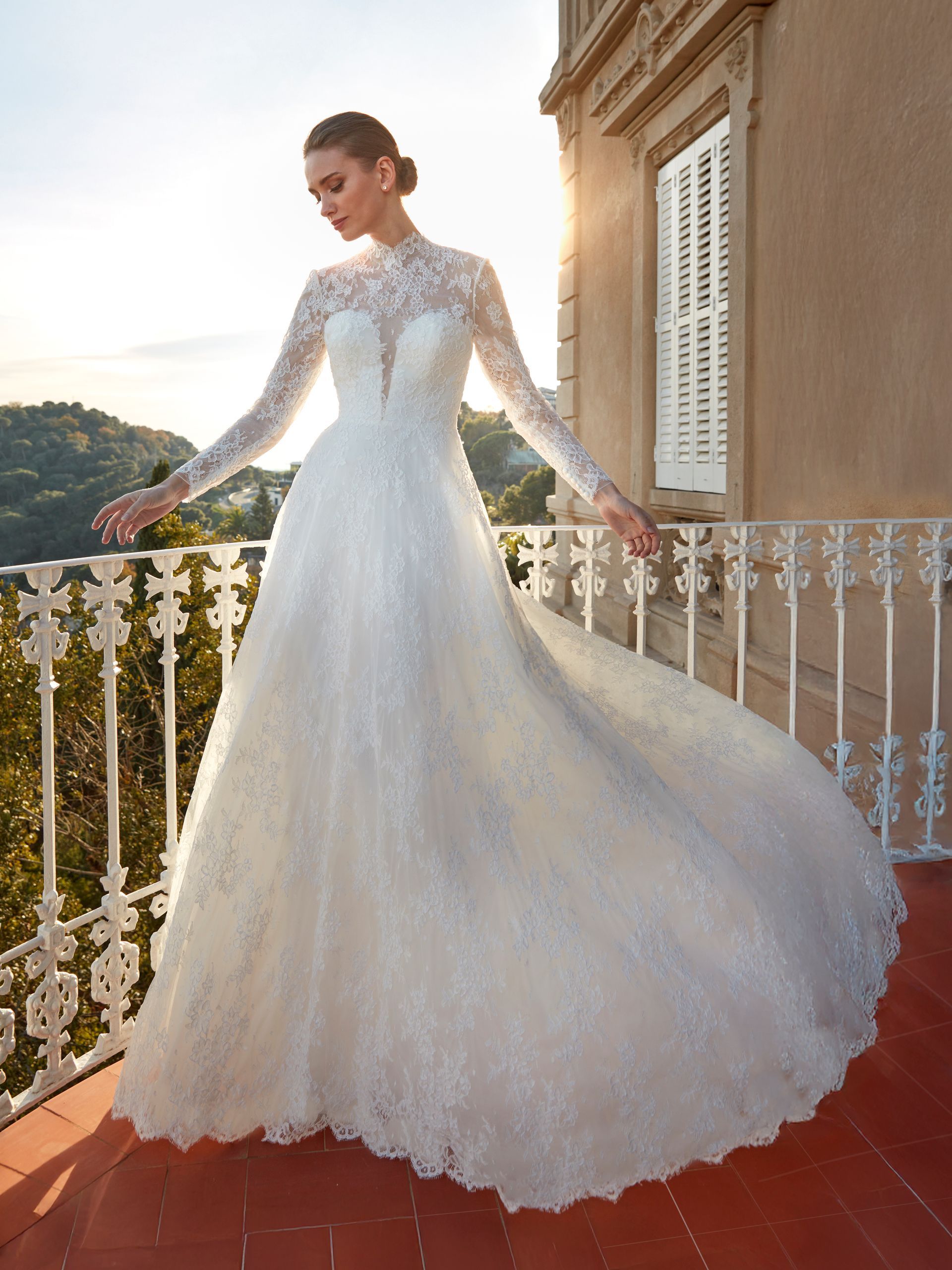 Sposa in abito di pizzo con maniche lunghe, in posa su un balcone.
