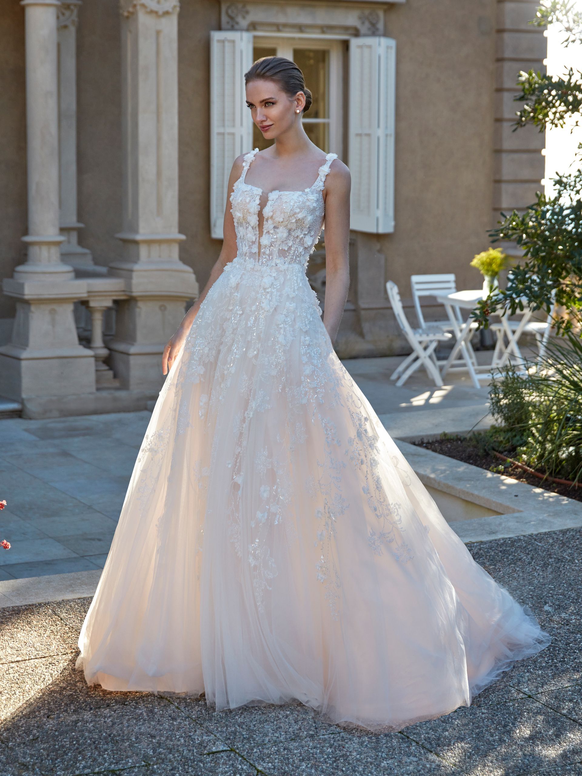 Donna in abito da sposa in posa all'aperto. Abito beige con corpetto floreale, schiena scoperta e gonna fluida.