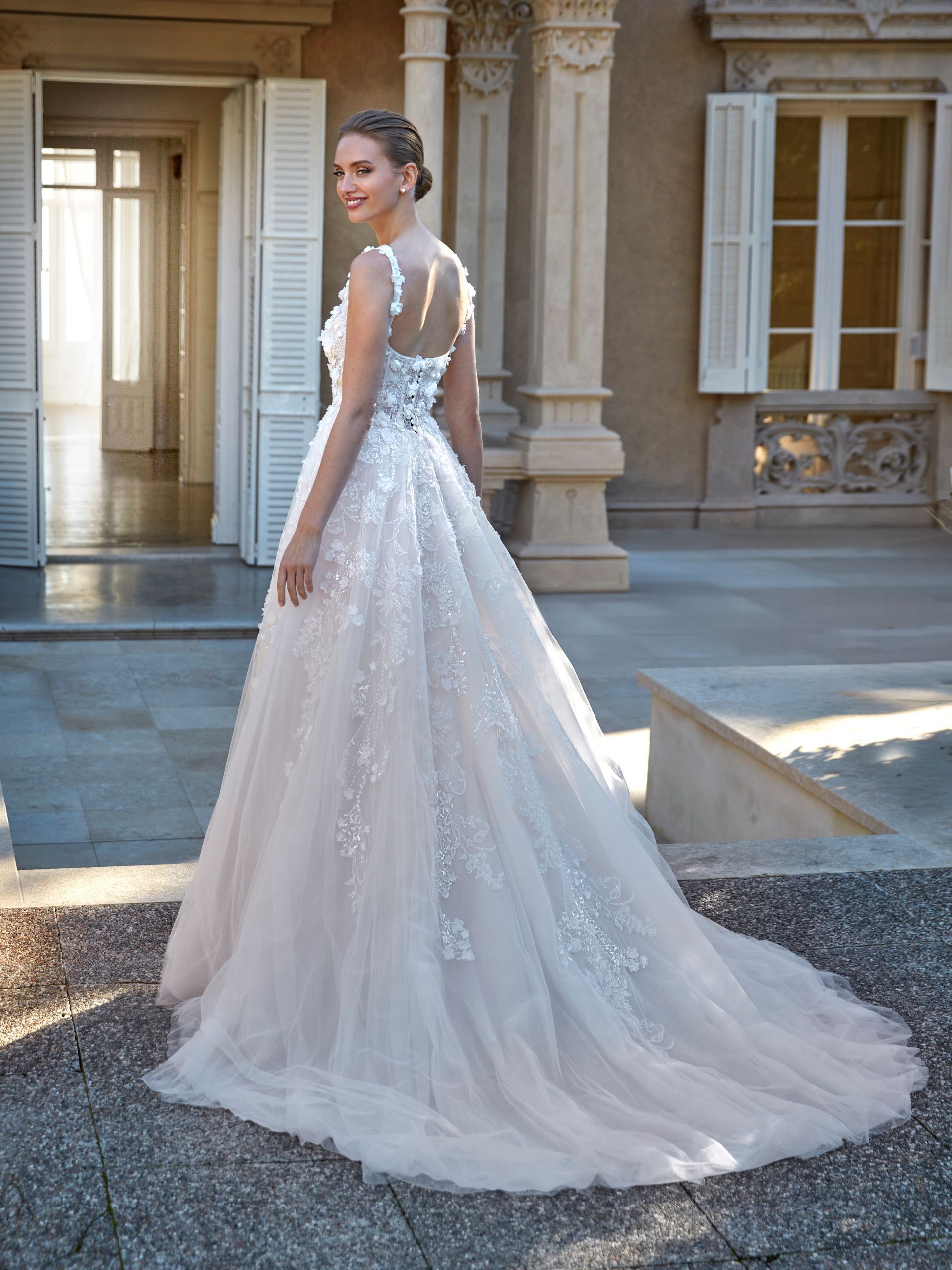 Sposa in abito bianco con dettagli floreali, sorridente all'aperto.