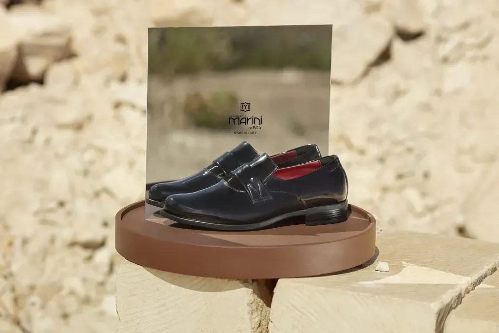 Un paio di scarpe eleganti nere esposte su un piedistallo marrone, con una scatola sullo sfondo, all'aperto.