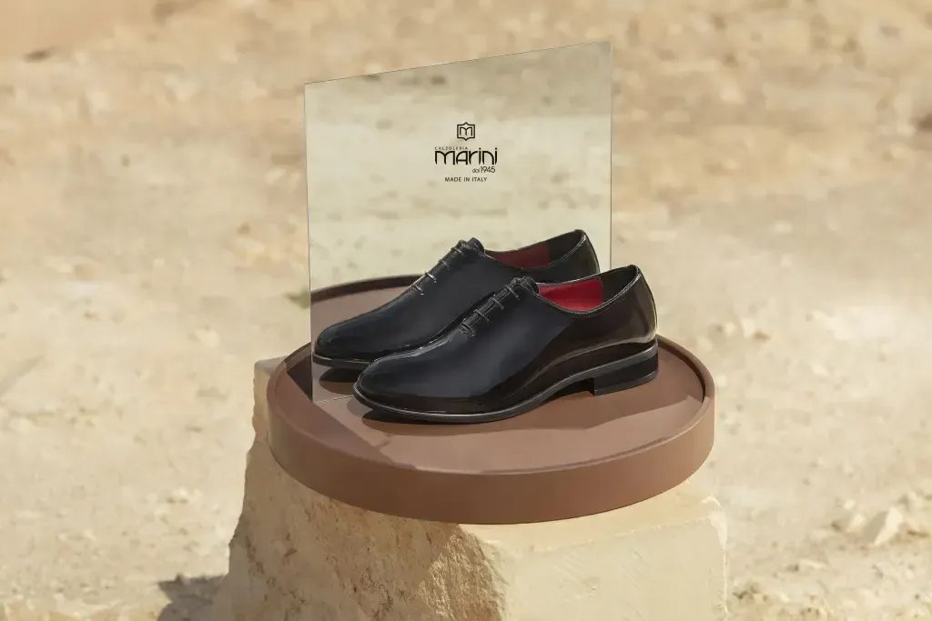 Scarpe eleganti nere su una zeppa circolare marrone, con un logo dietro, in un ambiente desertico.