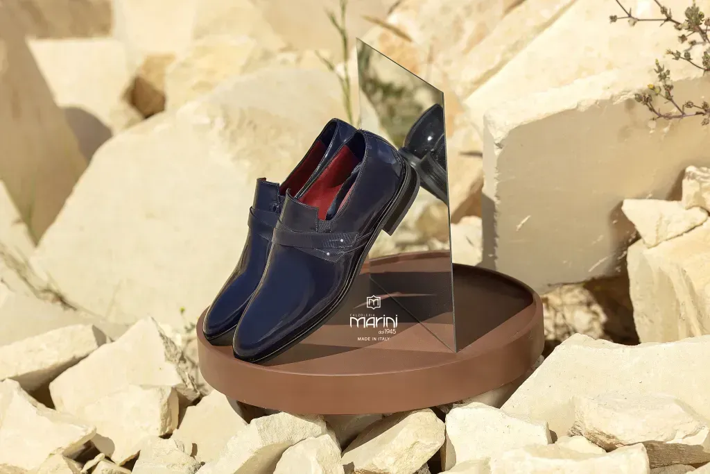 Mocassini in pelle blu esposti su un piedistallo marrone con specchio sullo sfondo di rocce bianche.