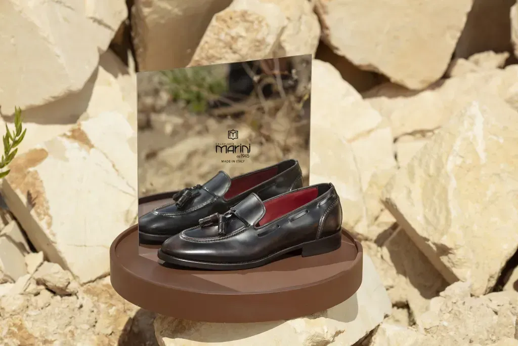 Mocassini in pelle nera su un supporto marrone, con logo, appoggiati sulle rocce.