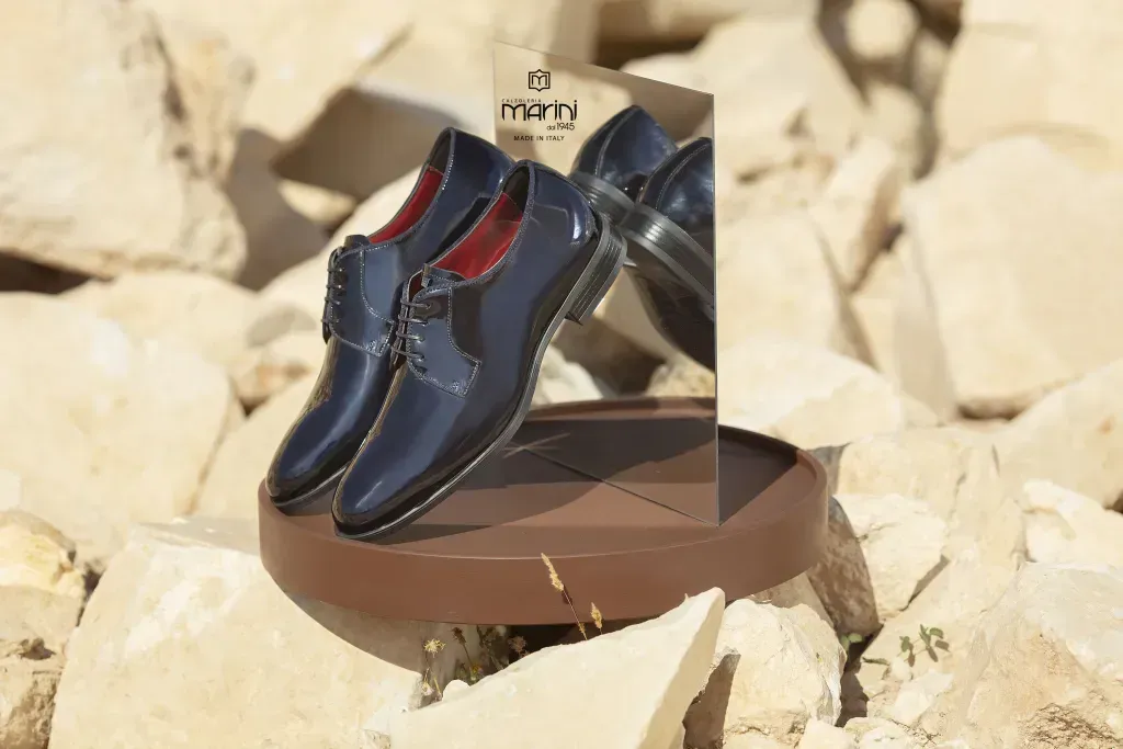 Scarpe eleganti da uomo blu lucido esposte su un espositore, tra rocce chiare esposte al sole.