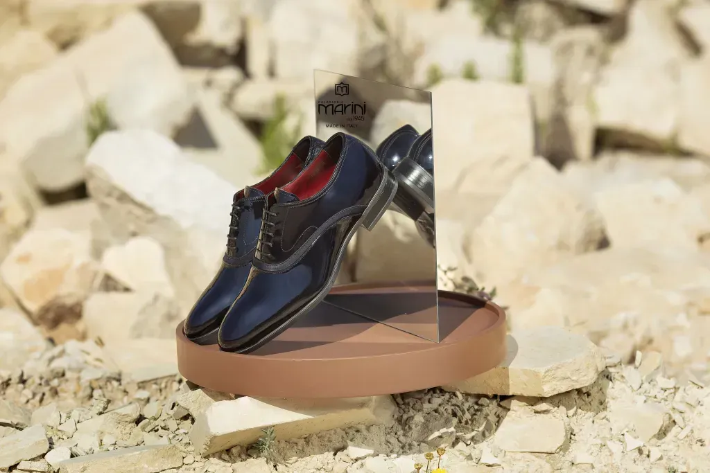 Un paio di scarpe eleganti blu su un piedistallo marrone, riflesse in un piccolo specchio, incastonate tra le rocce.