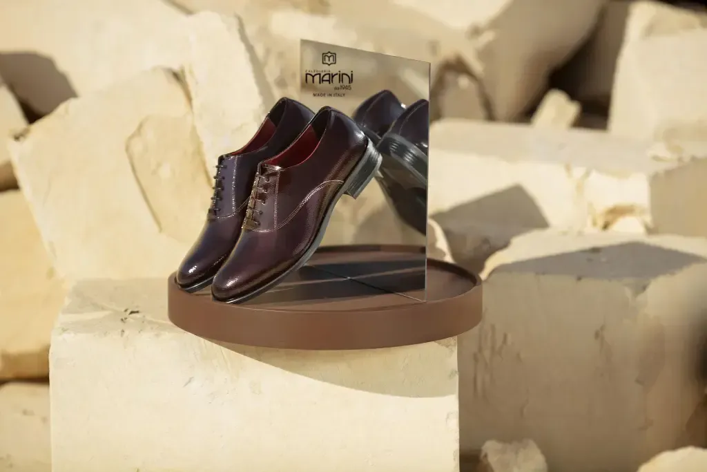 Un paio di scarpe in pelle marrone esposte su uno sfondo a specchio, appoggiate su una superficie in pietra.