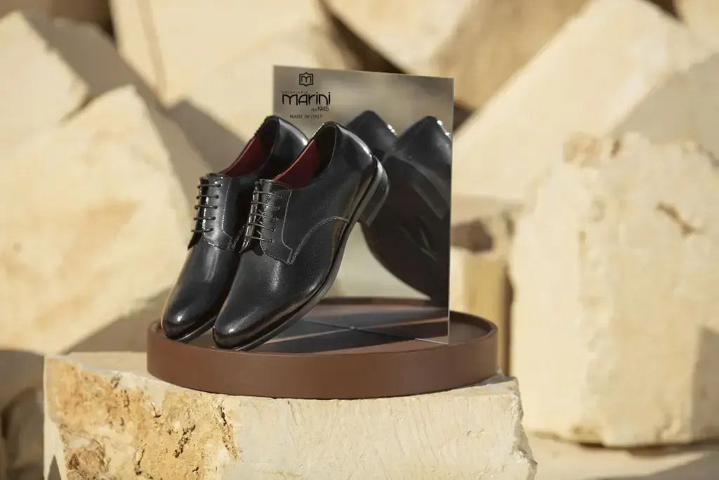 Scarpe eleganti nere con interno rosso su un supporto marrone, su uno sfondo di pietre chiare.