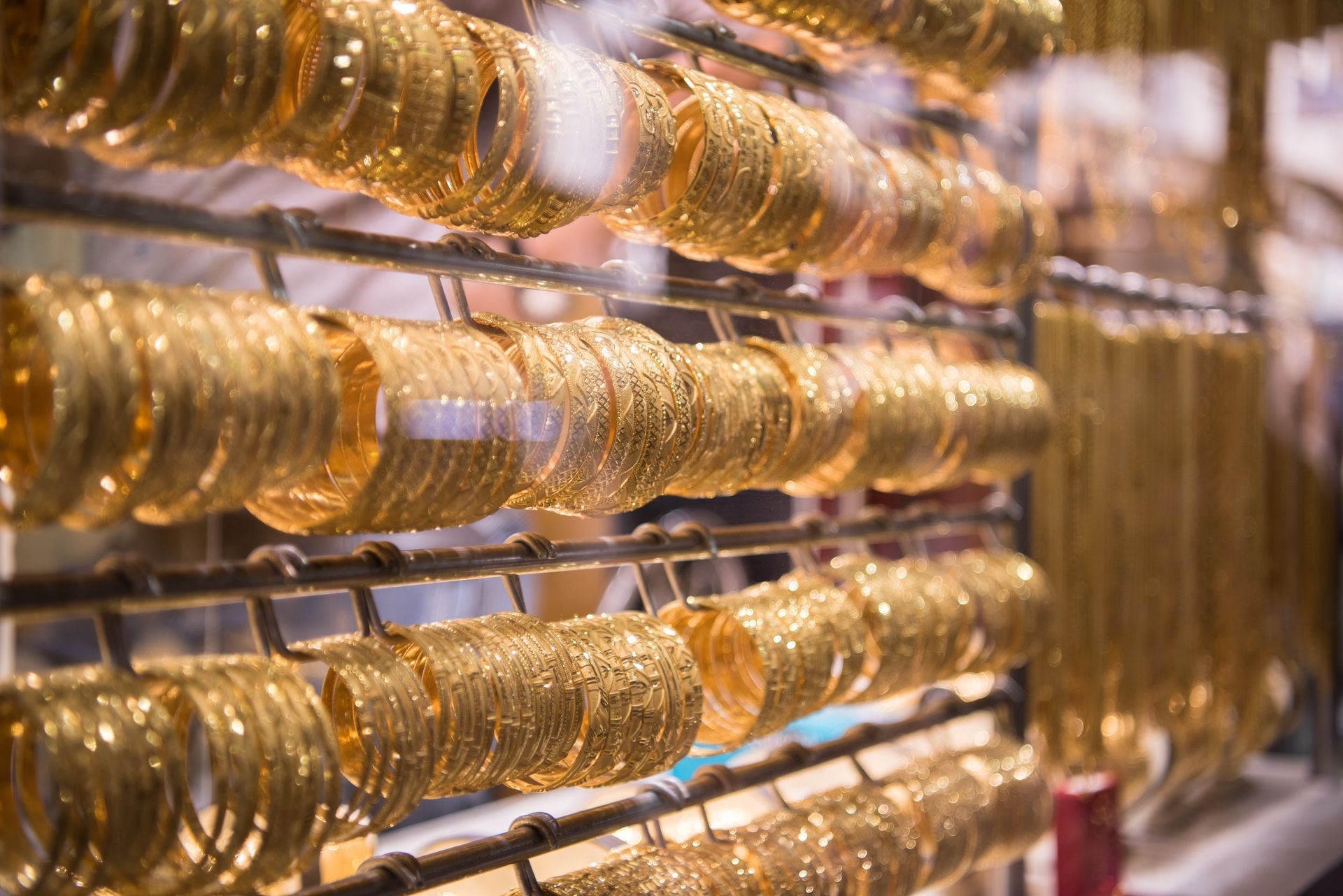 Rows of ornate gold bangles displayed on metal racks inside a jewelry store.