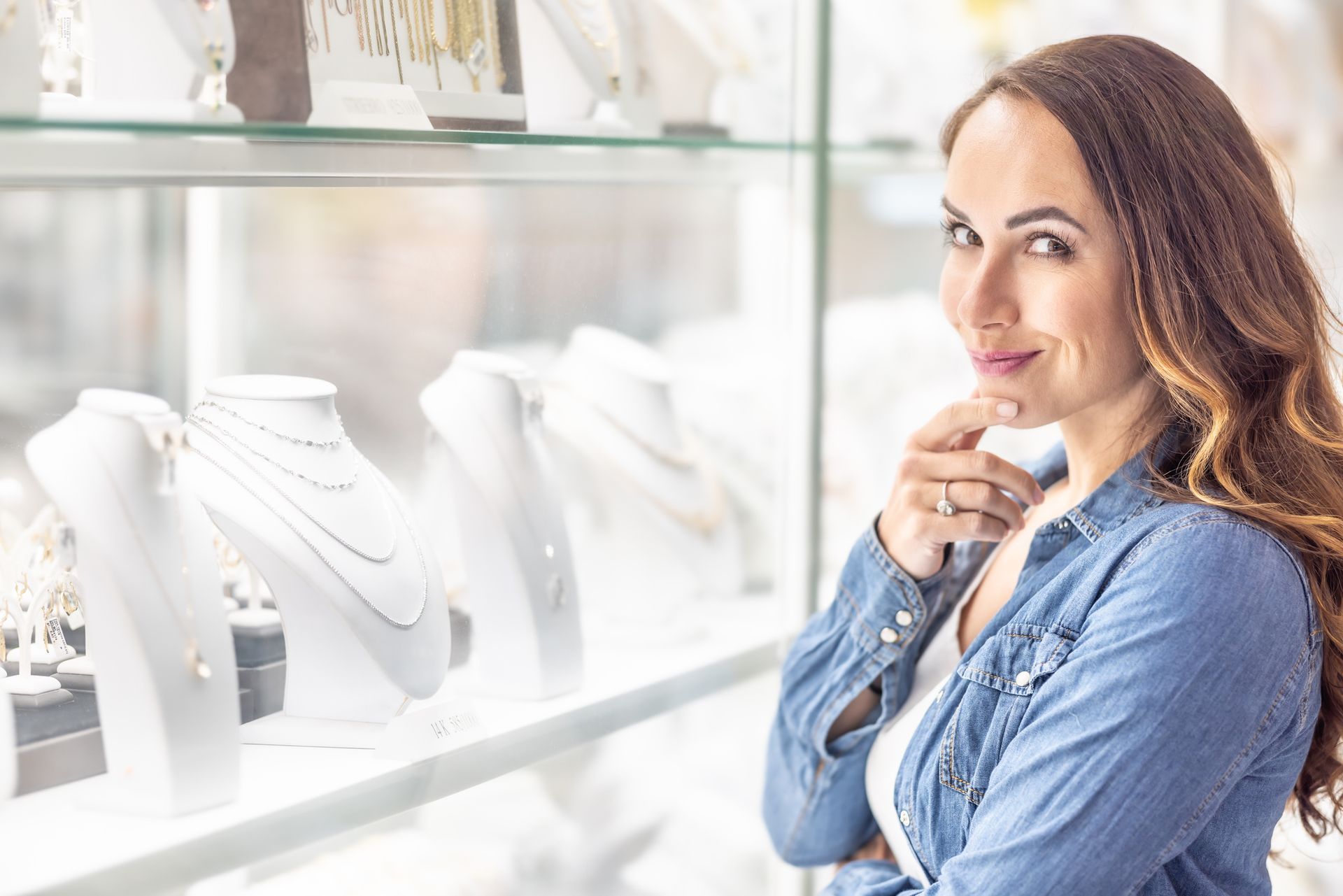 Young woman by jewelry window, gold and silver, confidently looking at the camera