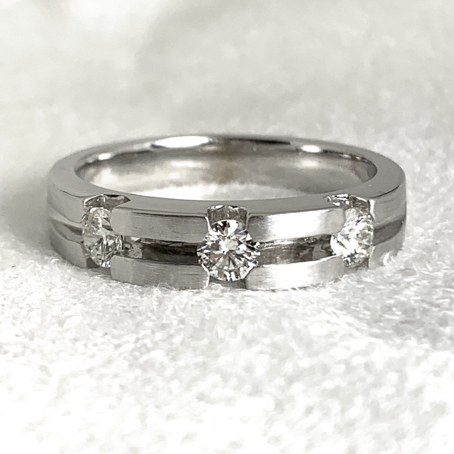 A white gold ring with three diamonds on a white surface.