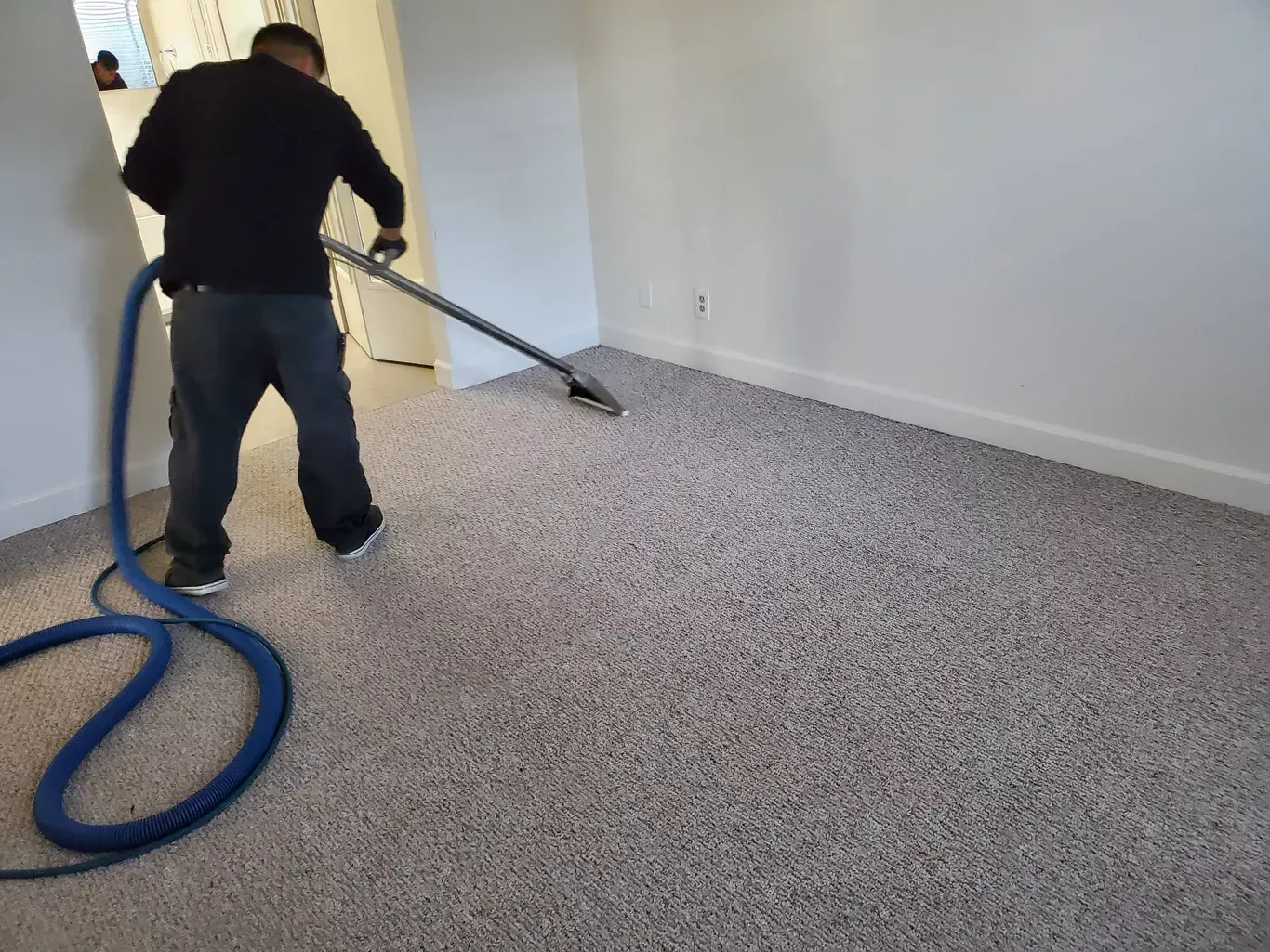 A man is cleaning a carpet with a vacuum cleaner.