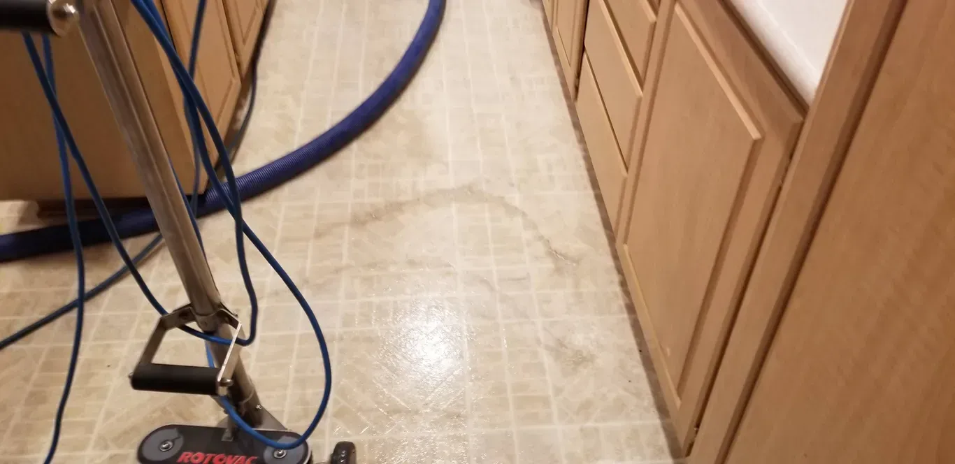 A vacuum cleaner is being used to clean a tile floor in a kitchen.