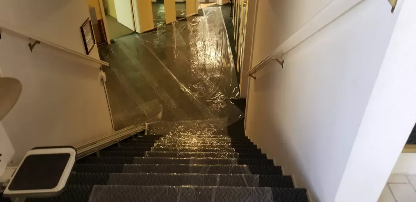 A flooded hallway with stairs leading up to it and water coming down the stairs.