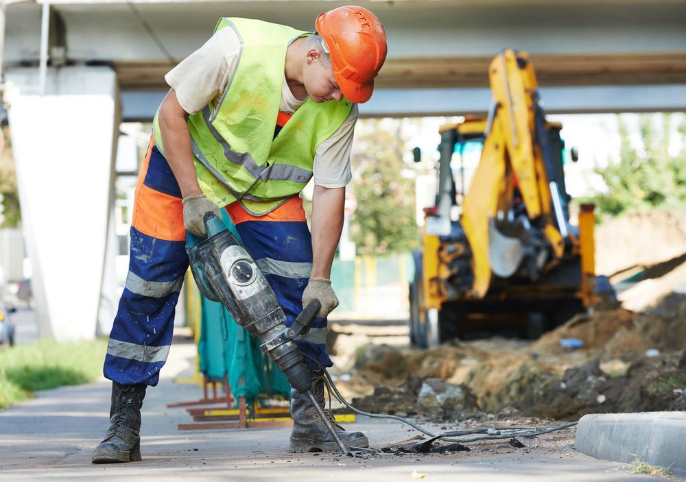 A construction worker is using a hammer to drill a hole in the ground.