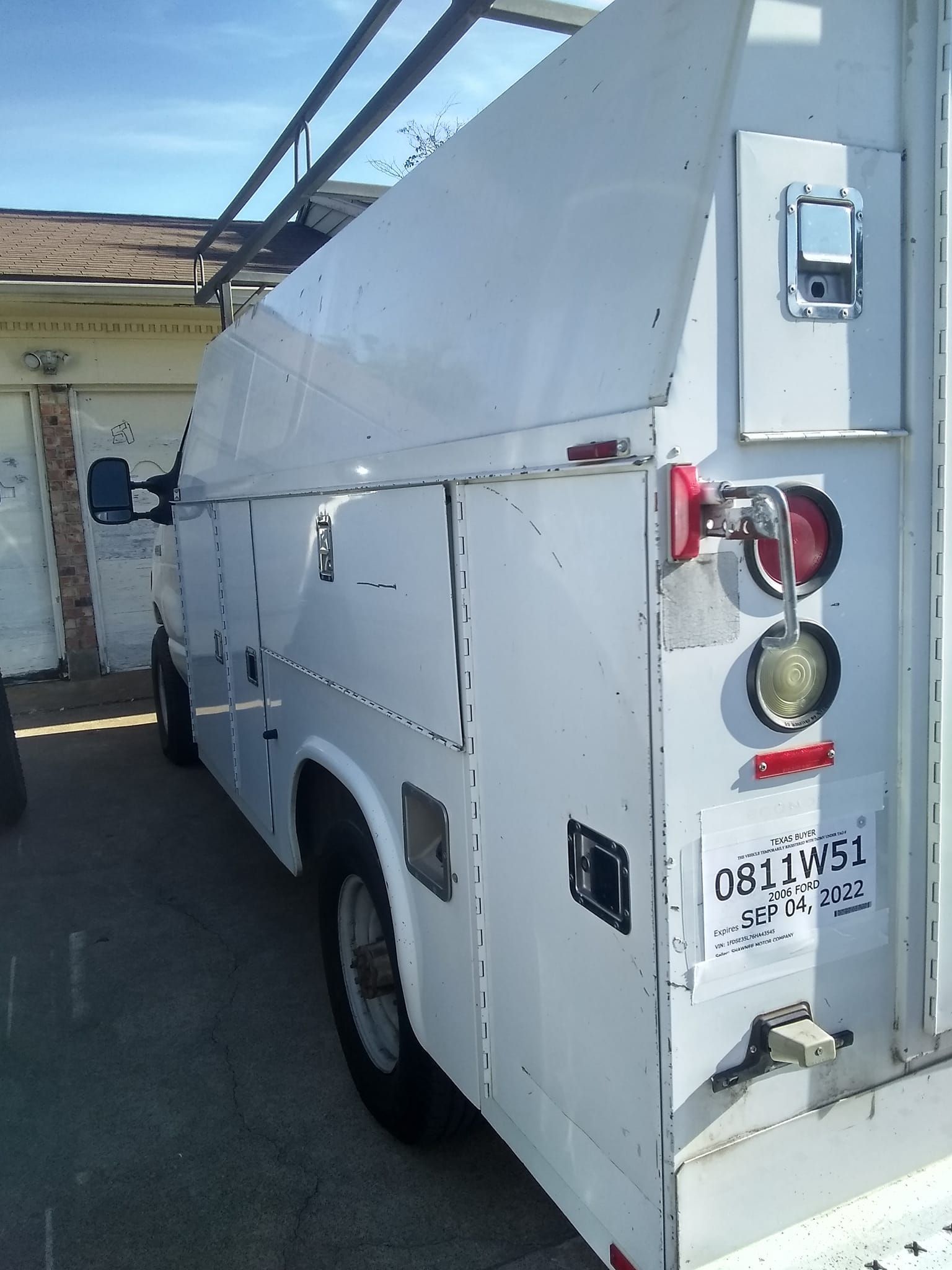 White utility van parked in a driveway beside a garage, viewed from the rear side.