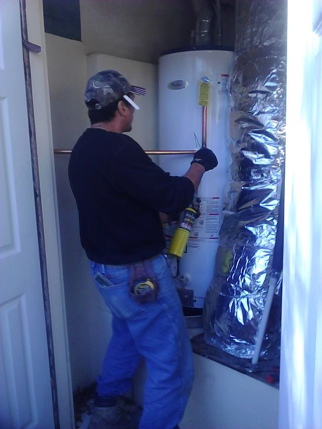 Technician using a drill beside a water heater in a utility closet, working on insulated ducting.
