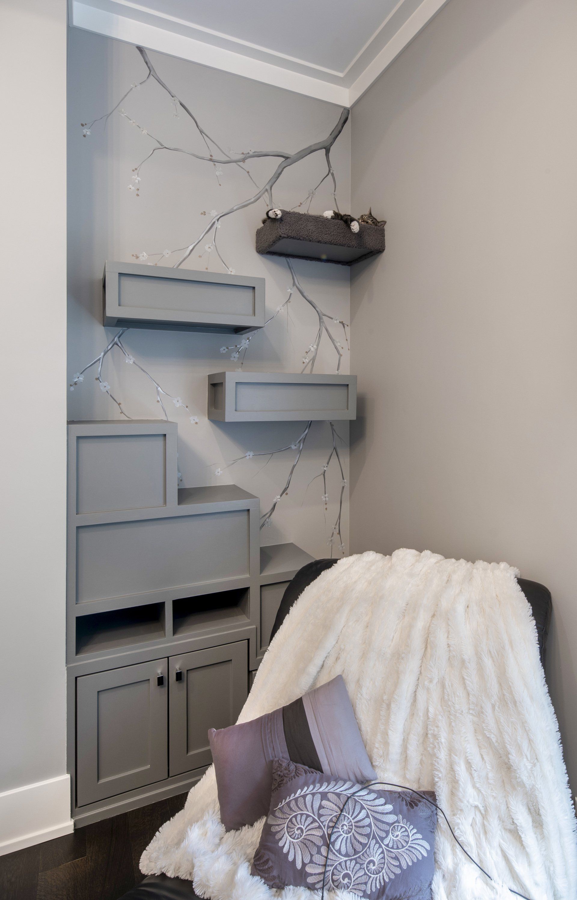 A chair with a blanket and pillows in a living room with shelves.