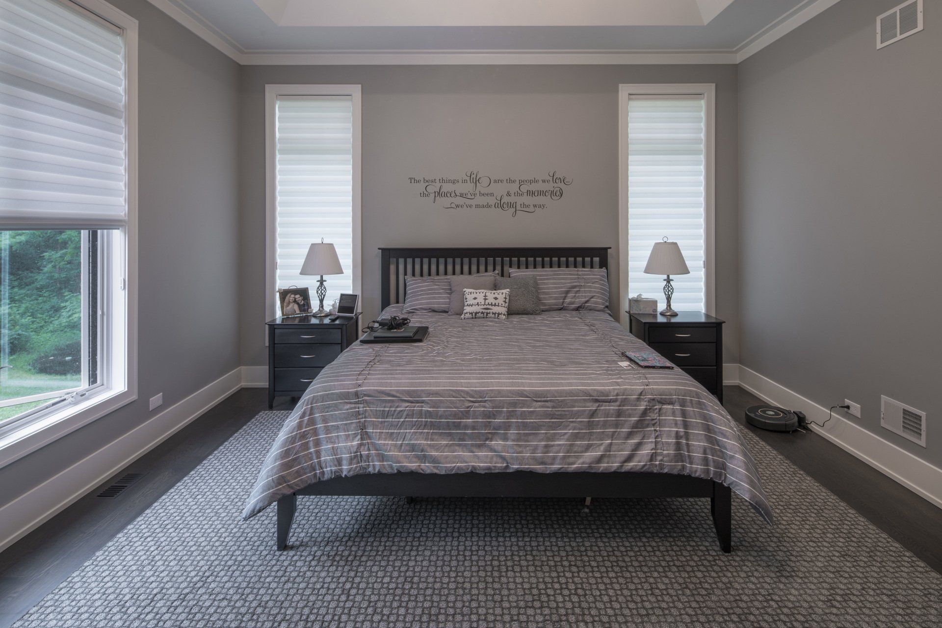 A bedroom with a bed , two nightstands , two windows and a rug.