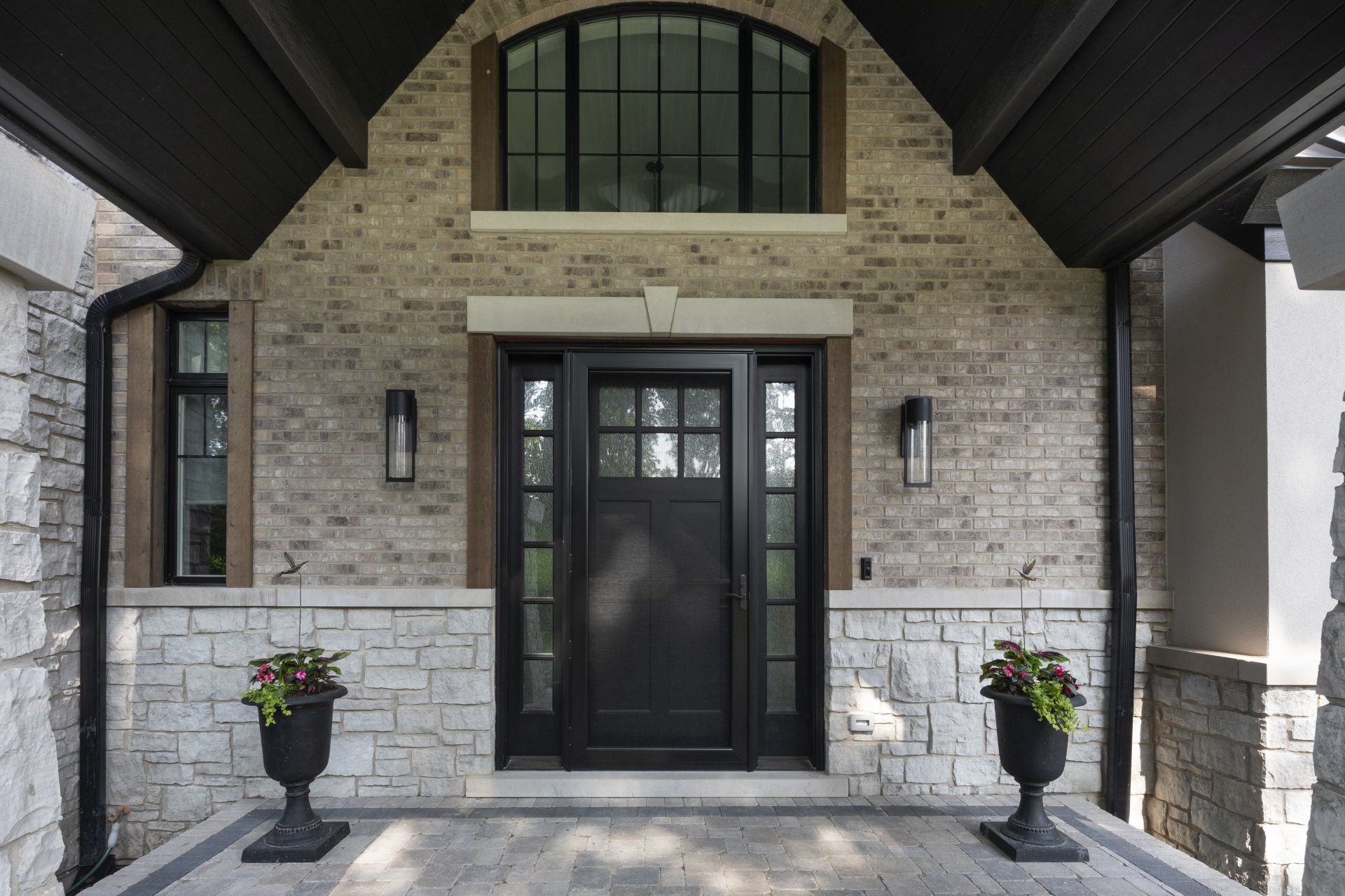 The front of a brick house with a black door and two potted plants in front of it.